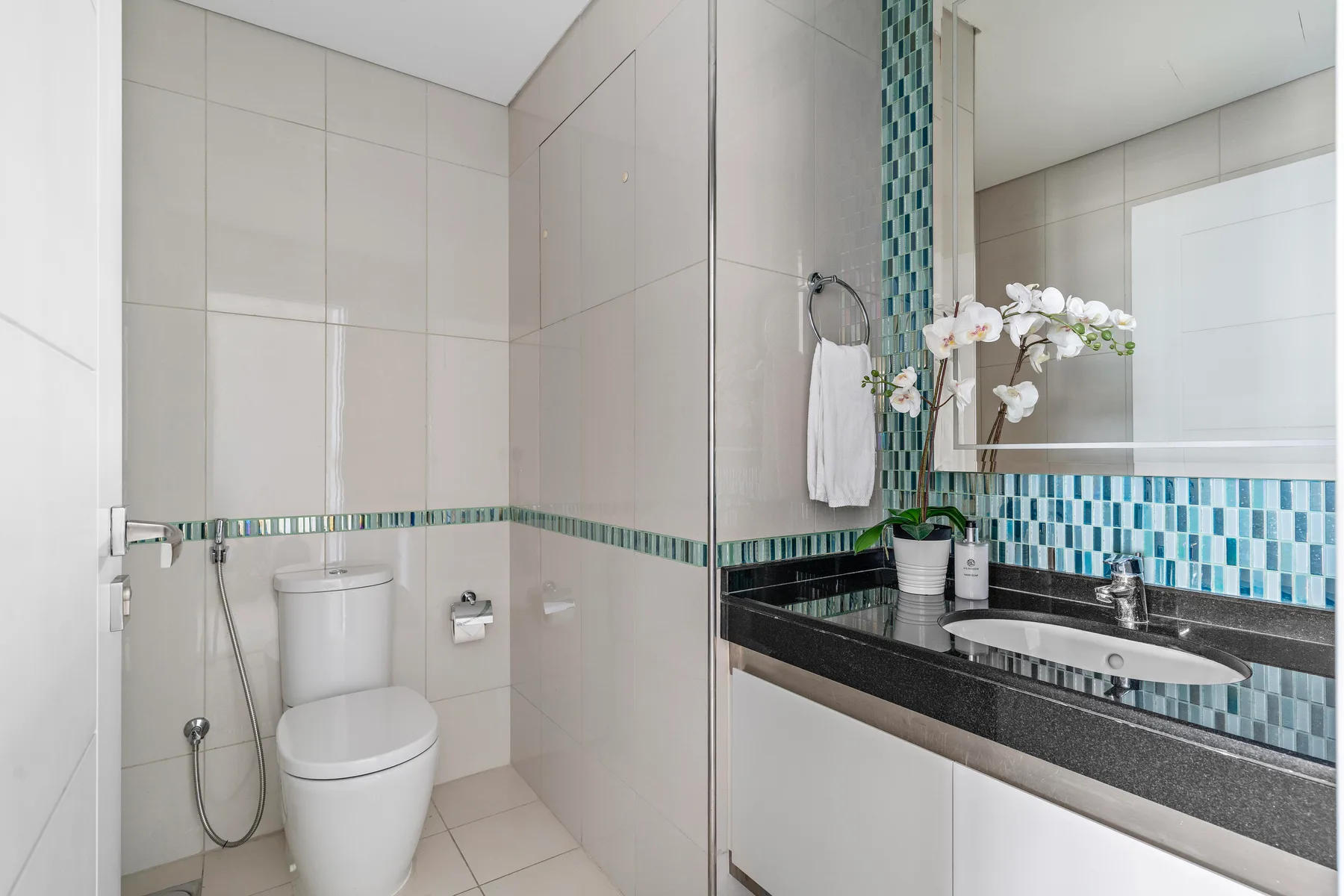 A tiled bathroom with a toilet, shower, and sink beneath a large mirror.