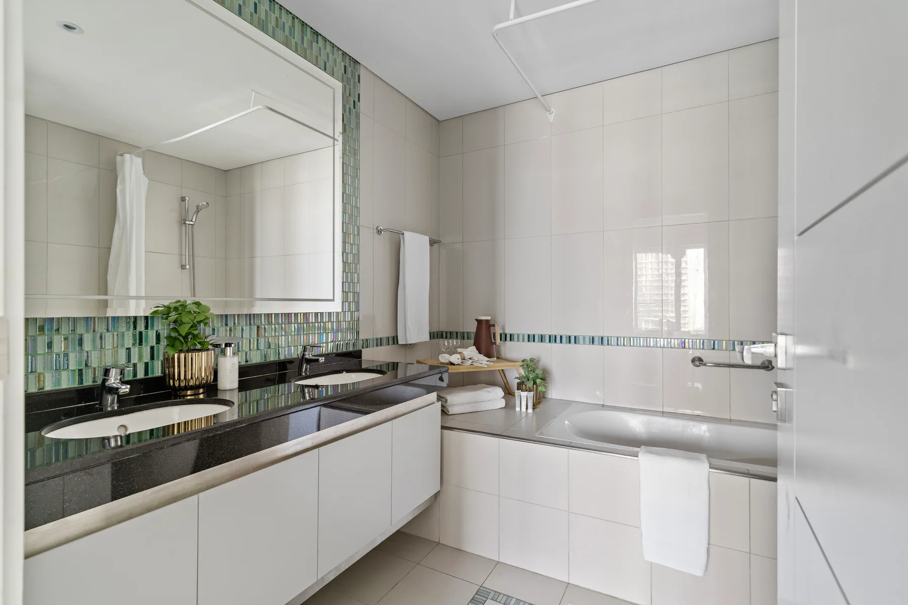 A bright tiled bathroom with a bathtub, shower, and long vanity.