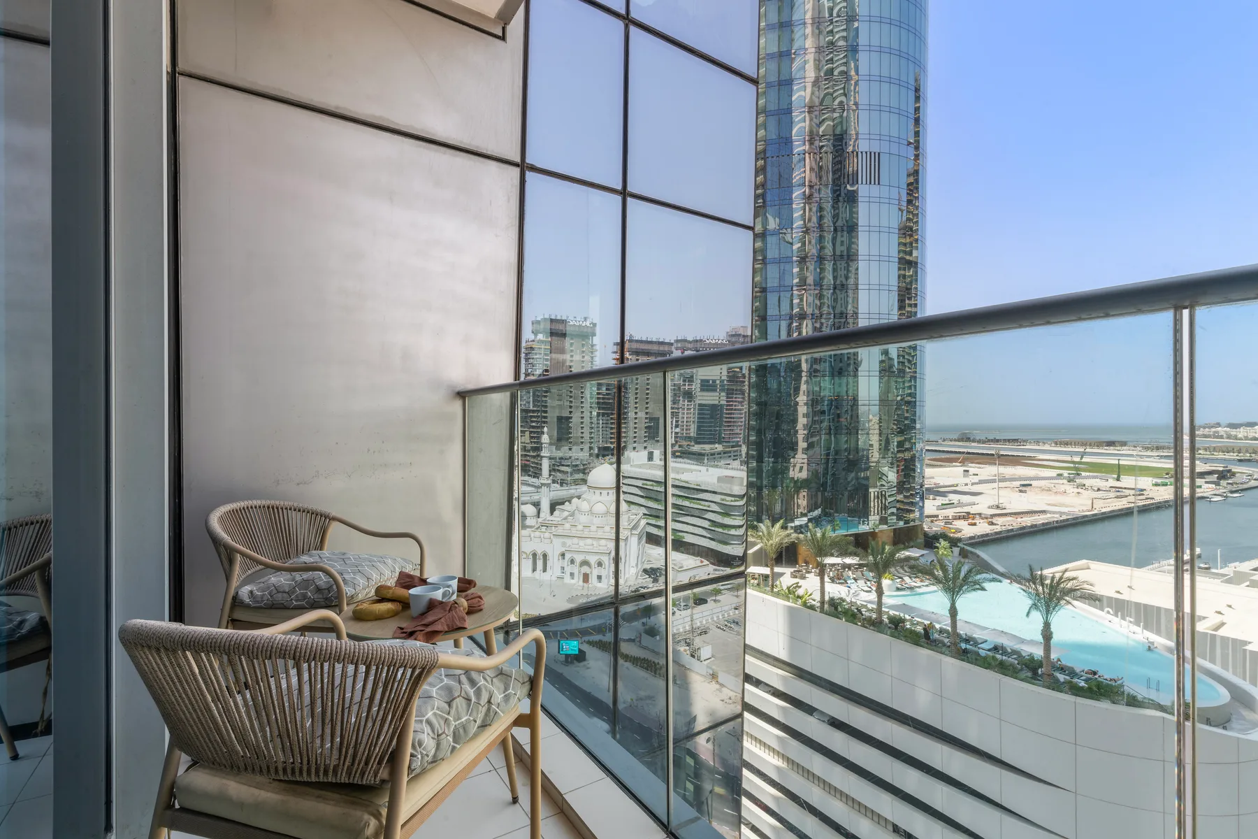 A balcony seating area overlooks a glass-fronted high-rise and the surrounding city.