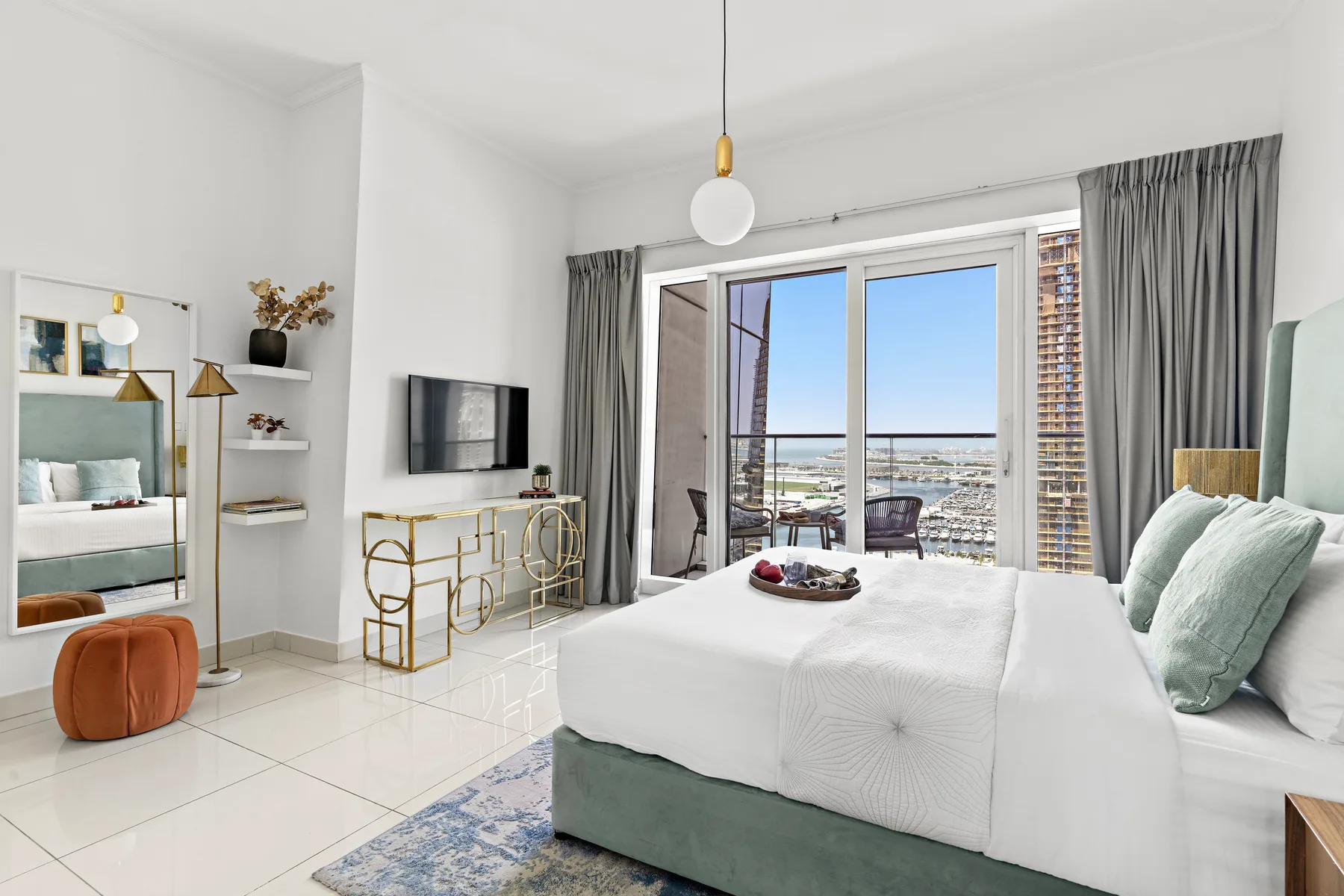 A bright bedroom with a bed, television, and large windows overlooking the city.