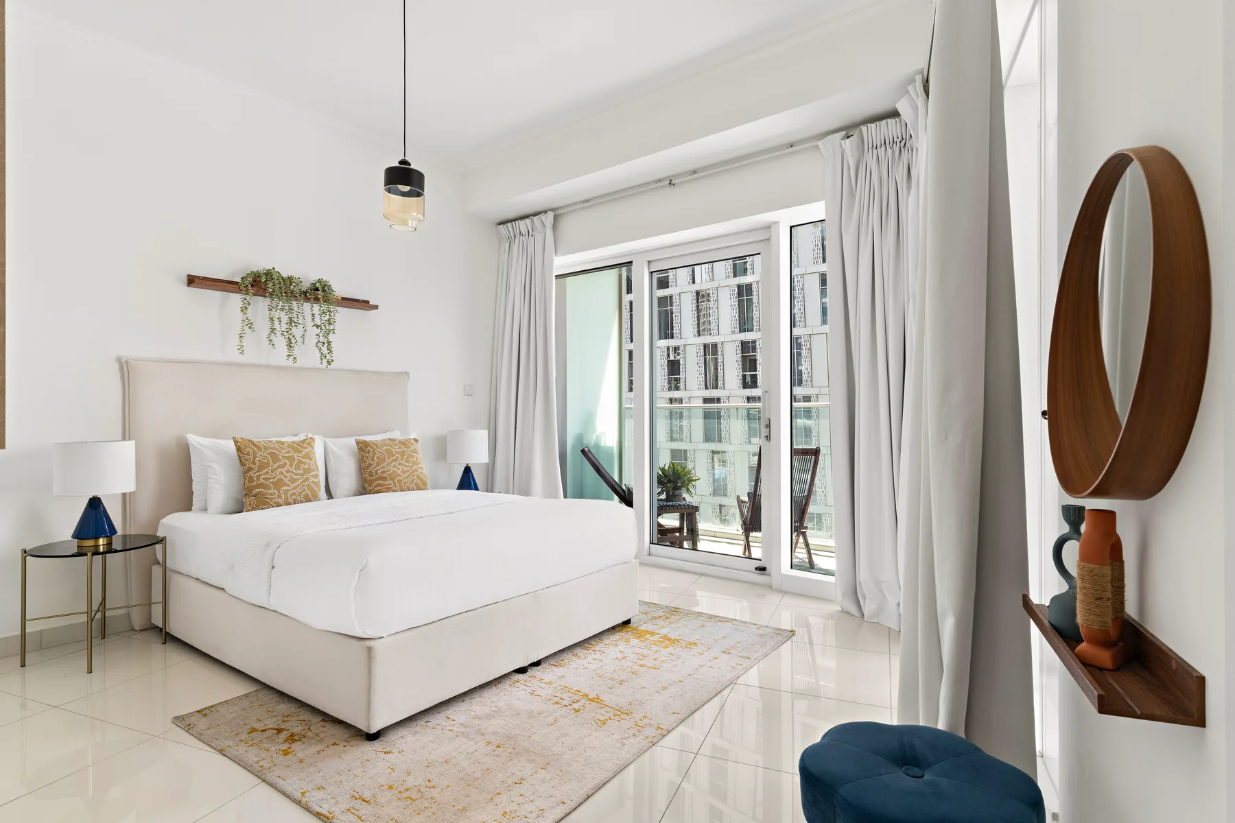 A bright bedroom with a large bed beside a curtained window.