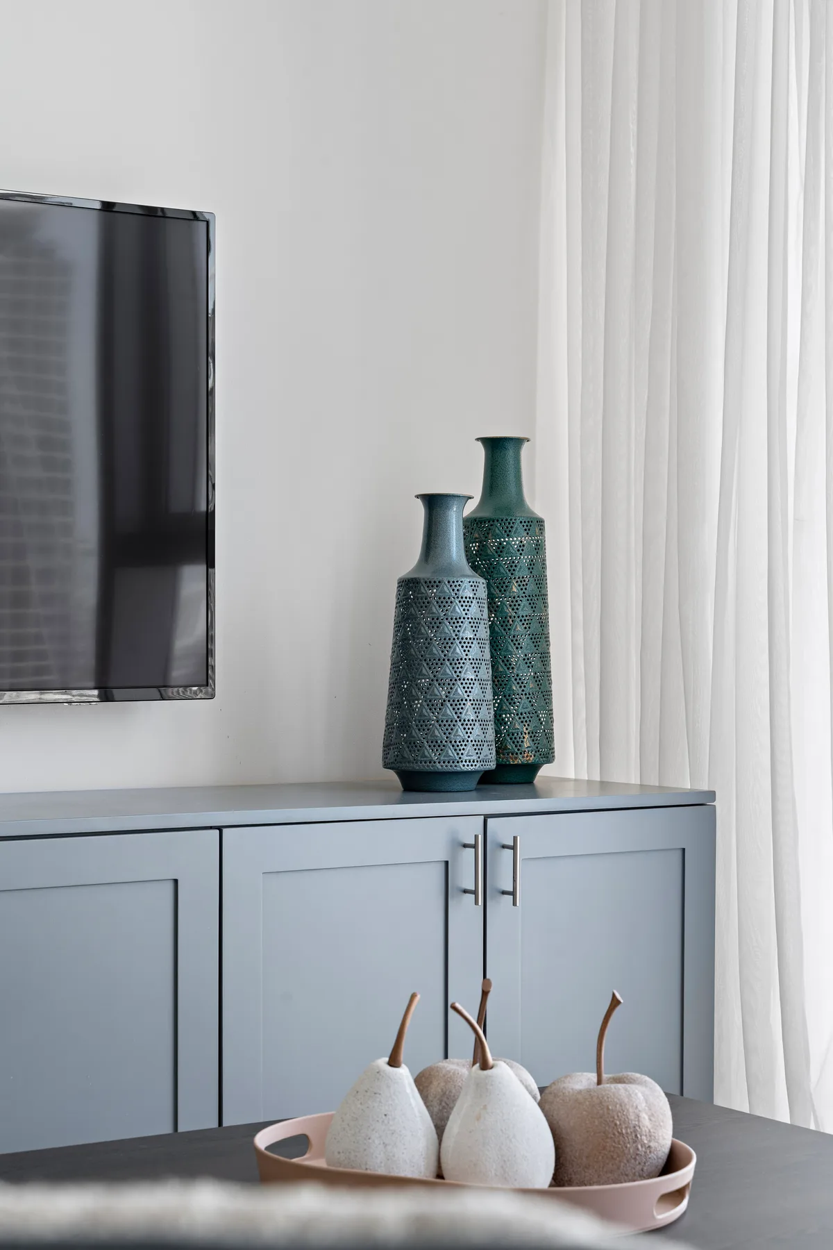 A living room with a television above a blue cabinet and decorative vases.