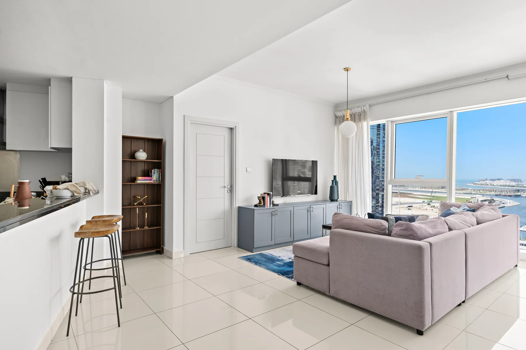 Bright open-plan living room with a kitchen counter and large windows overlooking the water.