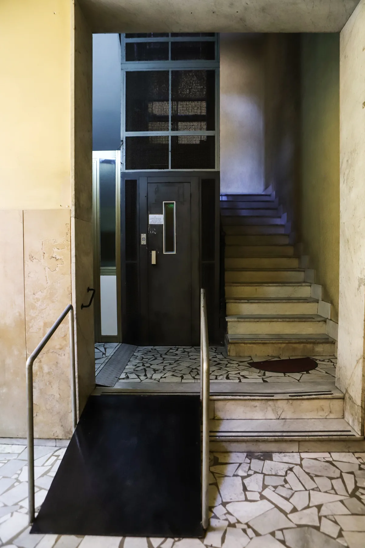 A building entrance with a dark door, patterned floor, and stairs.