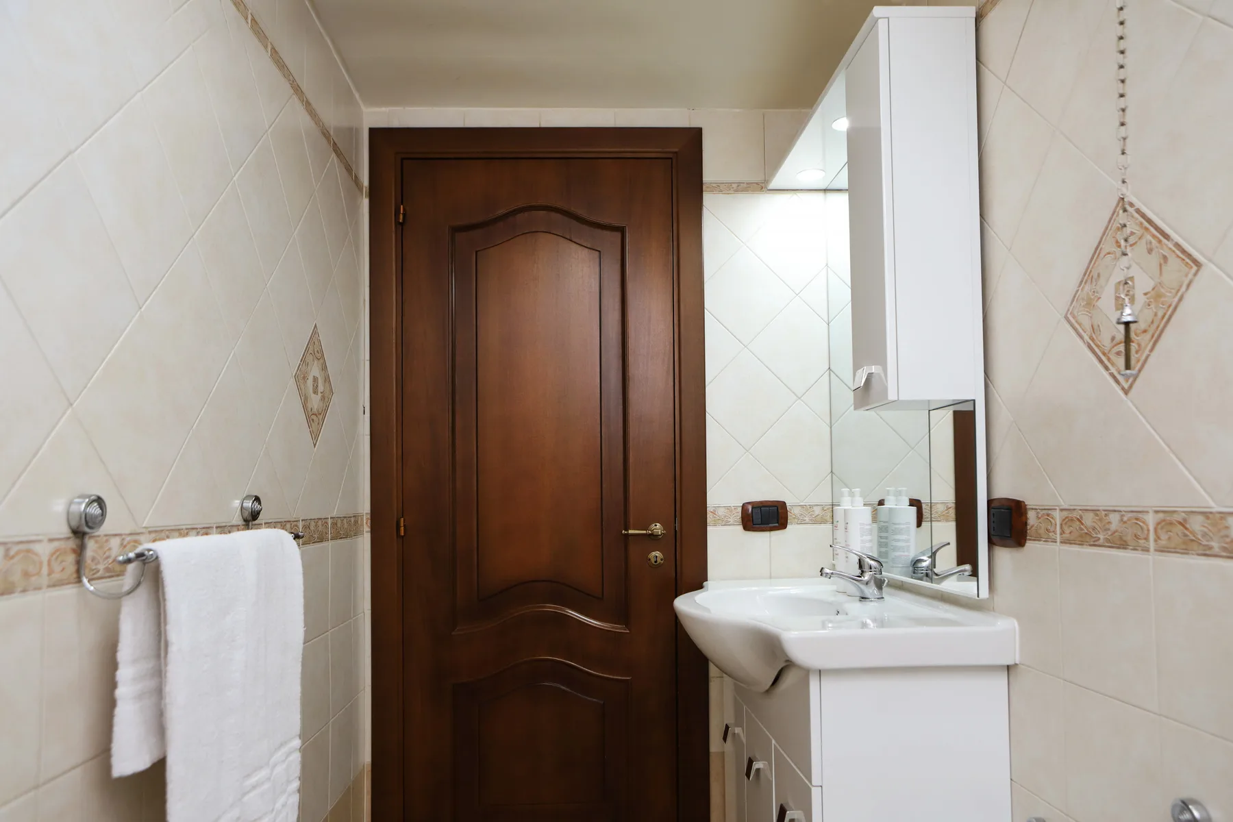 A tiled bathroom with a sink, mirror cabinet, and wooden door.