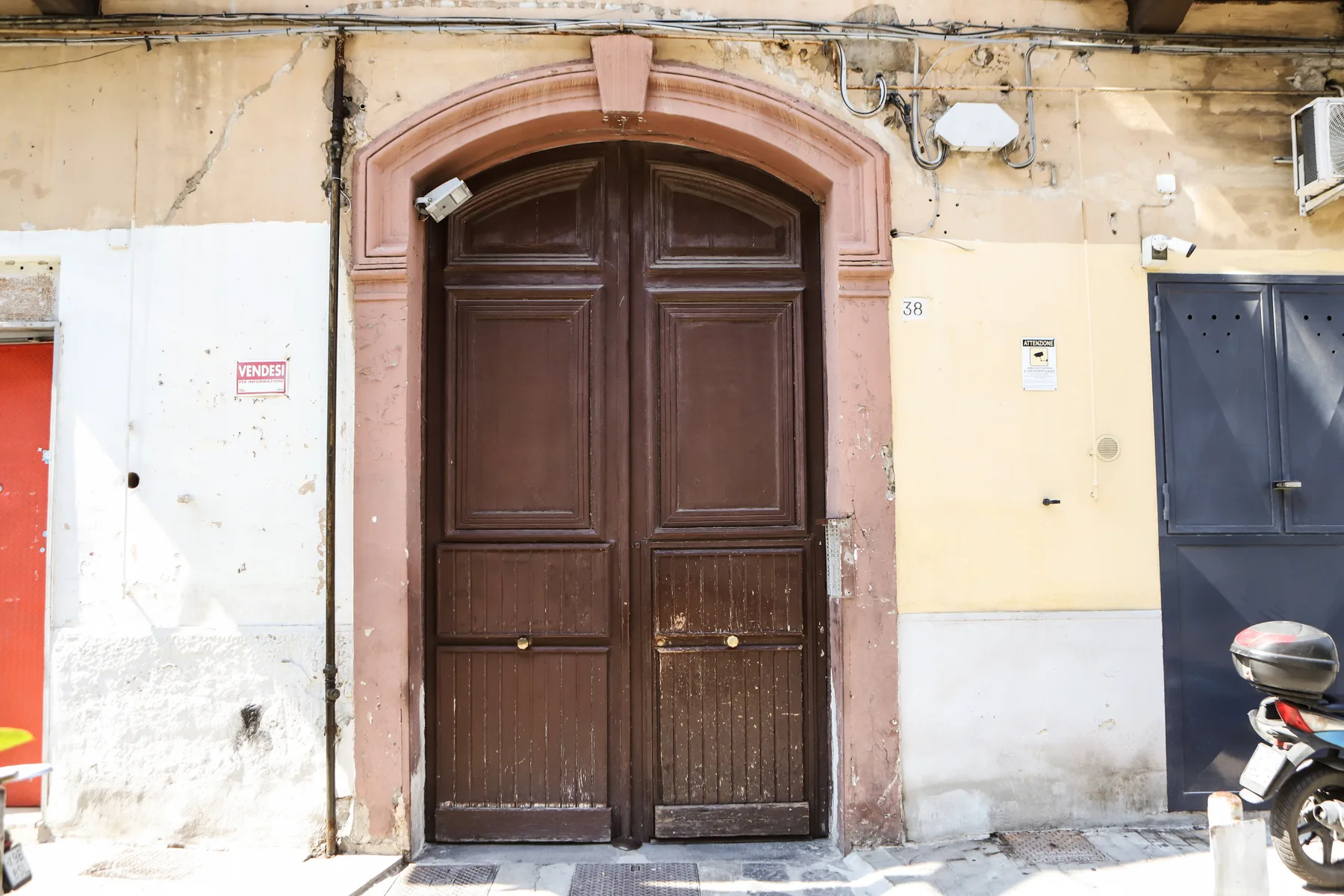 A large wooden double door sits within an arched entrance in a weathered exterior wall.