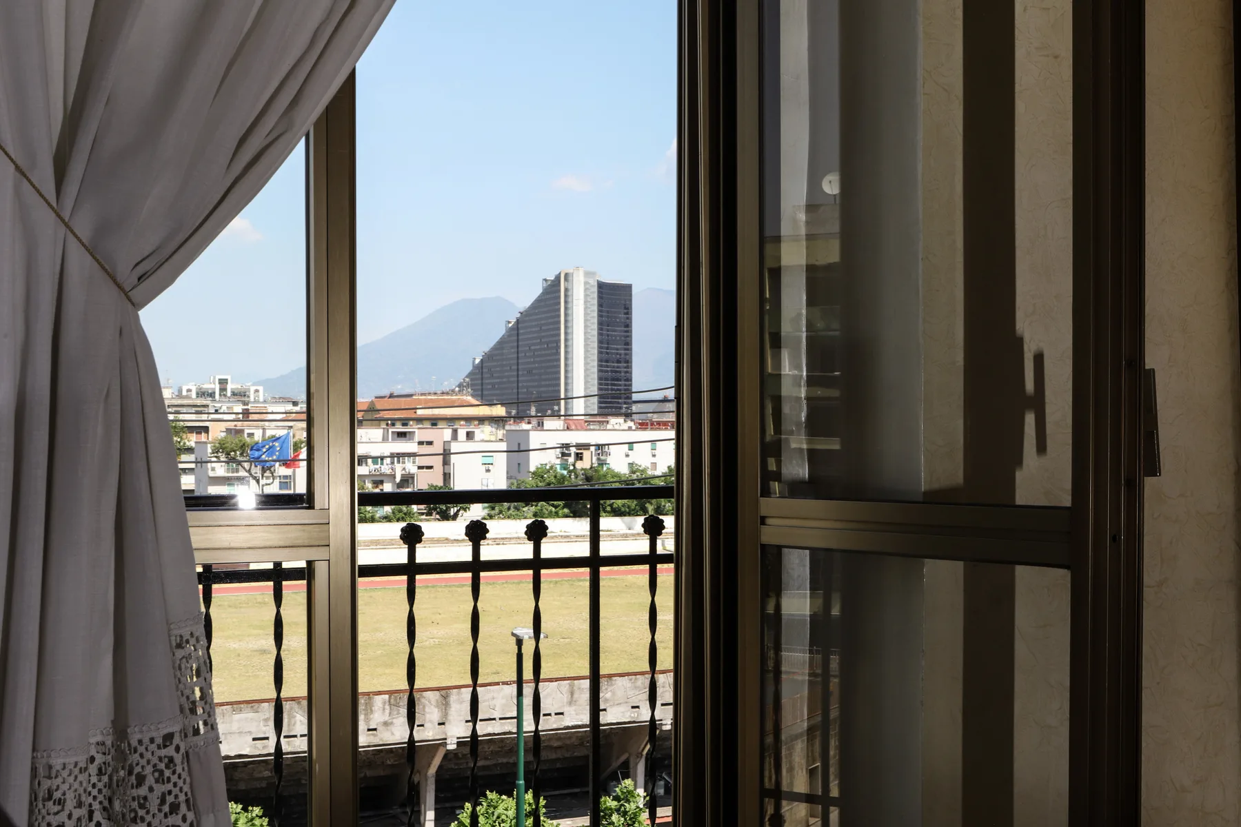 A window overlooks city buildings, a distant mountain, and a balcony railing.