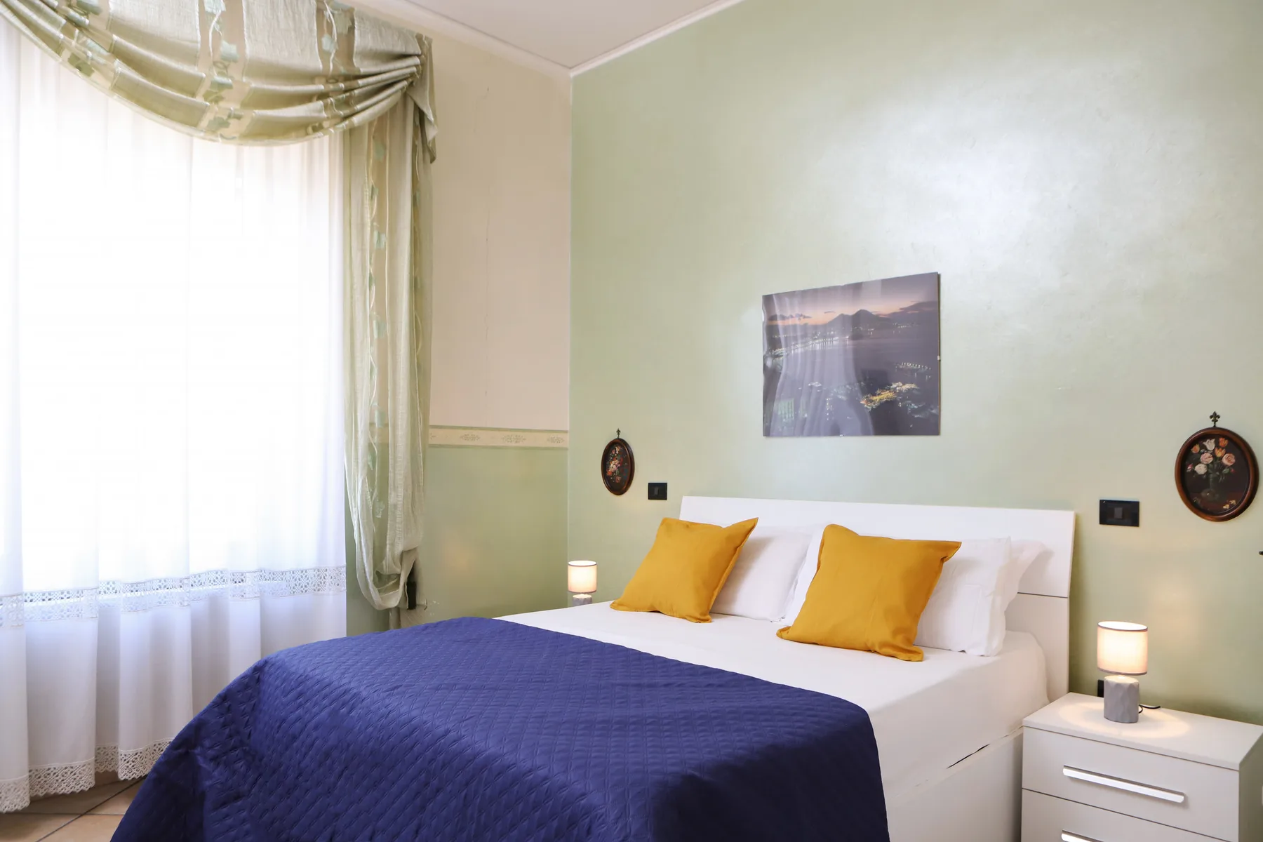A bedroom with a neatly made bed, colorful pillows, and a large window.
