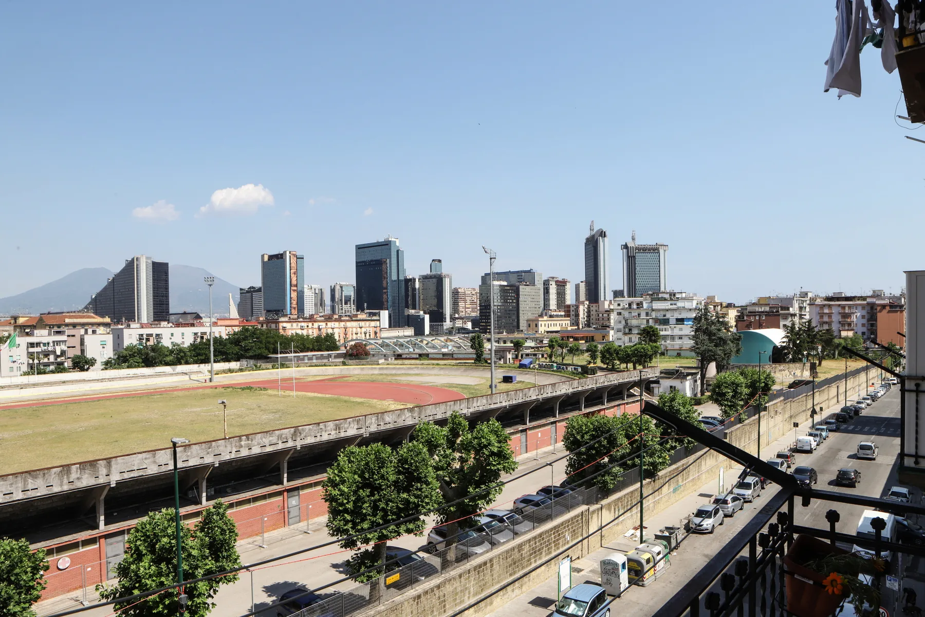 An urban cityscape with a broad sports field and modern buildings in the distance.