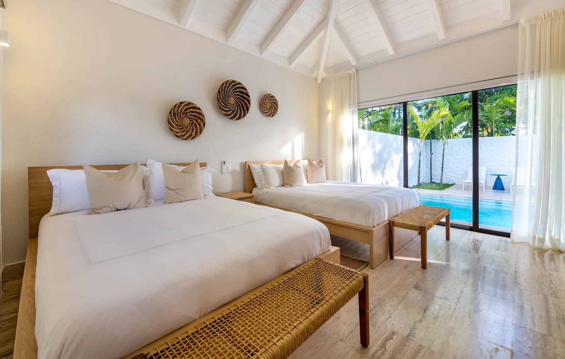 A bright bedroom with two beds and glass doors opening to a pool.