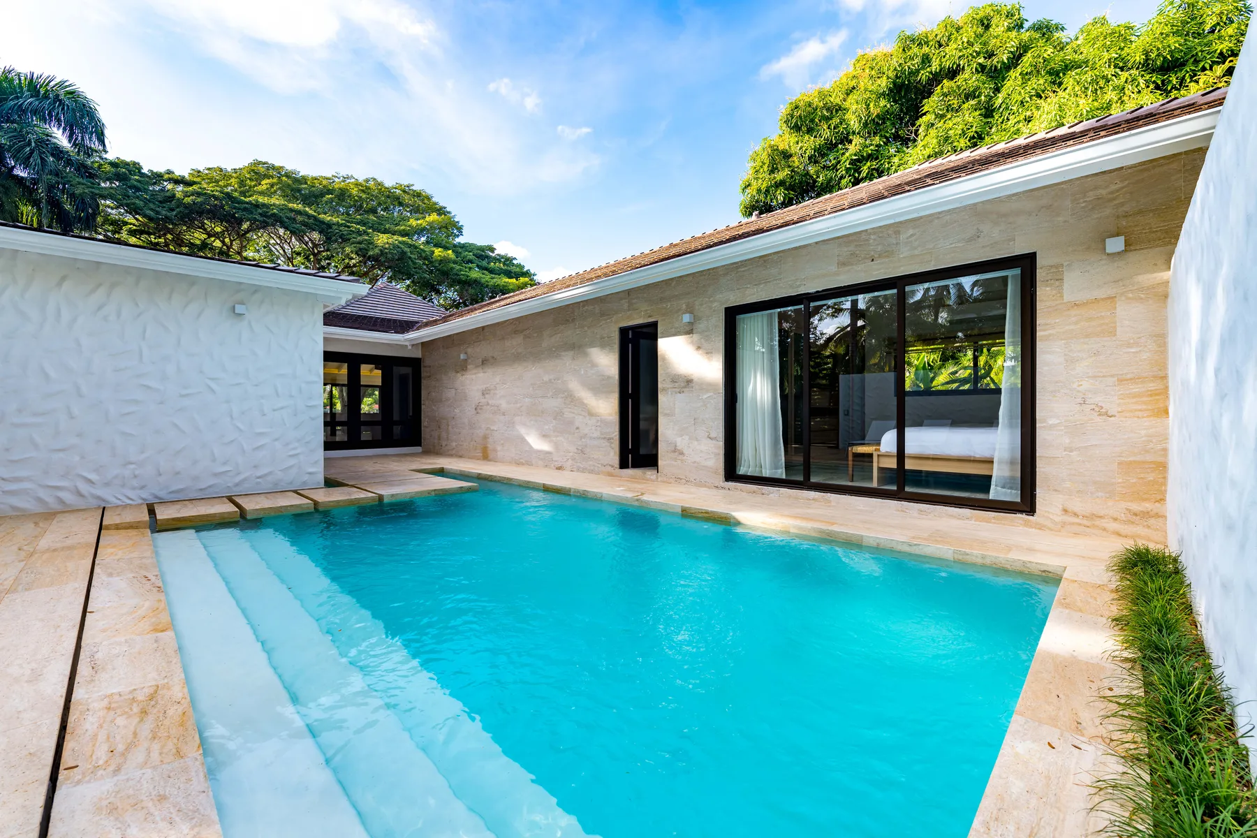 A swimming pool beside a modern house, with glass doors opening onto the patio.