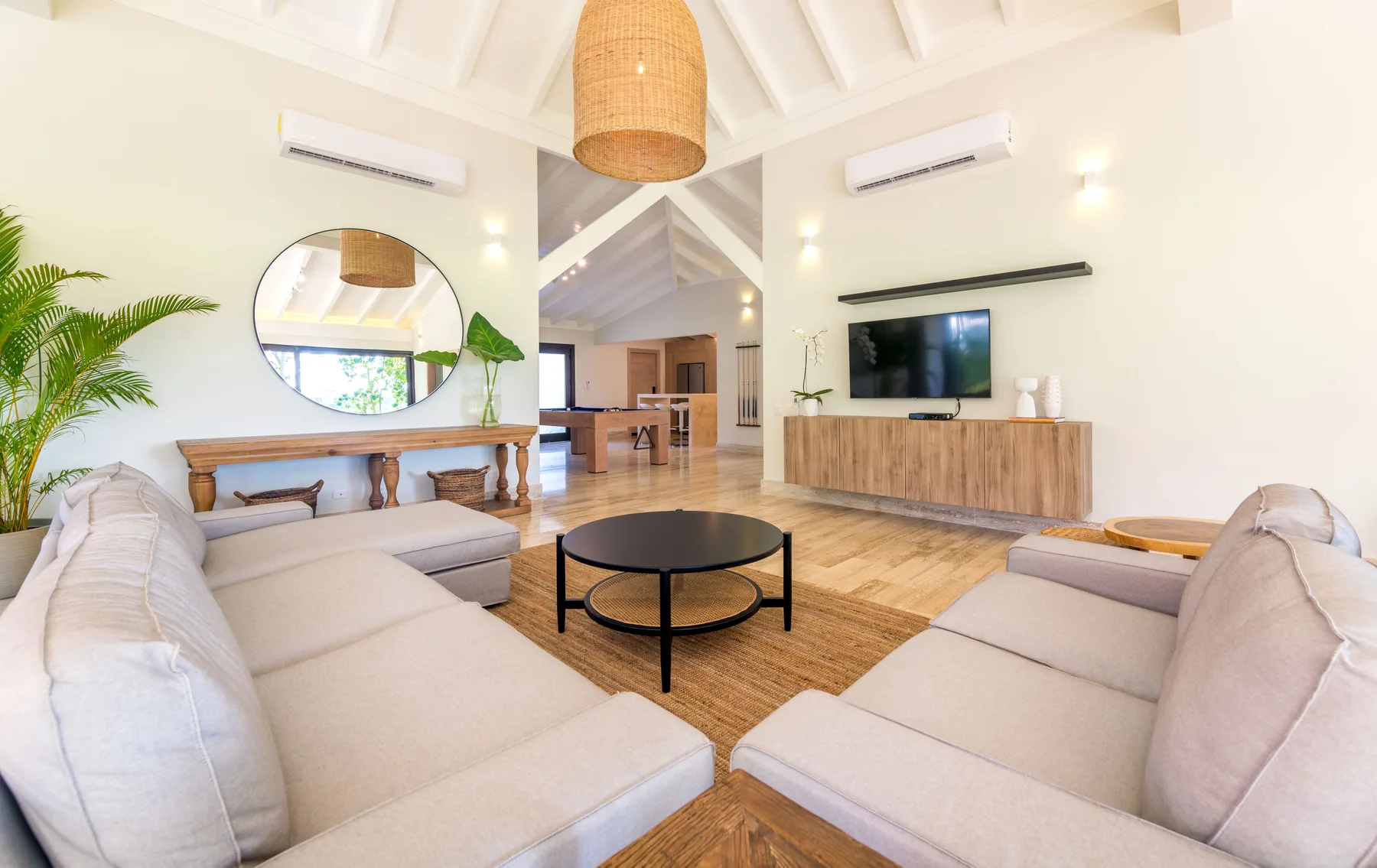 A bright living room with pale seating, a round coffee table, and a television.