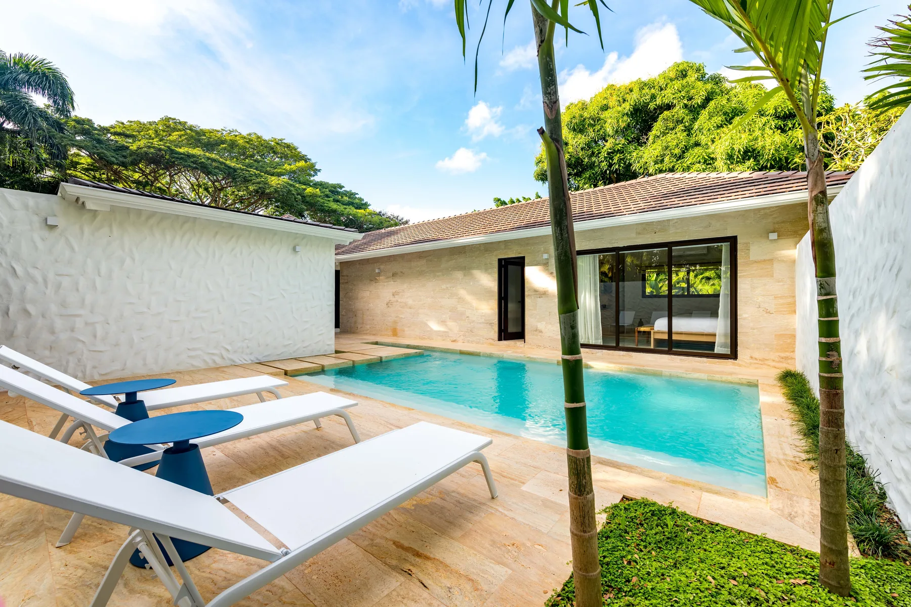 An outdoor swimming pool beside a light-colored house, with lounge seating on the patio.