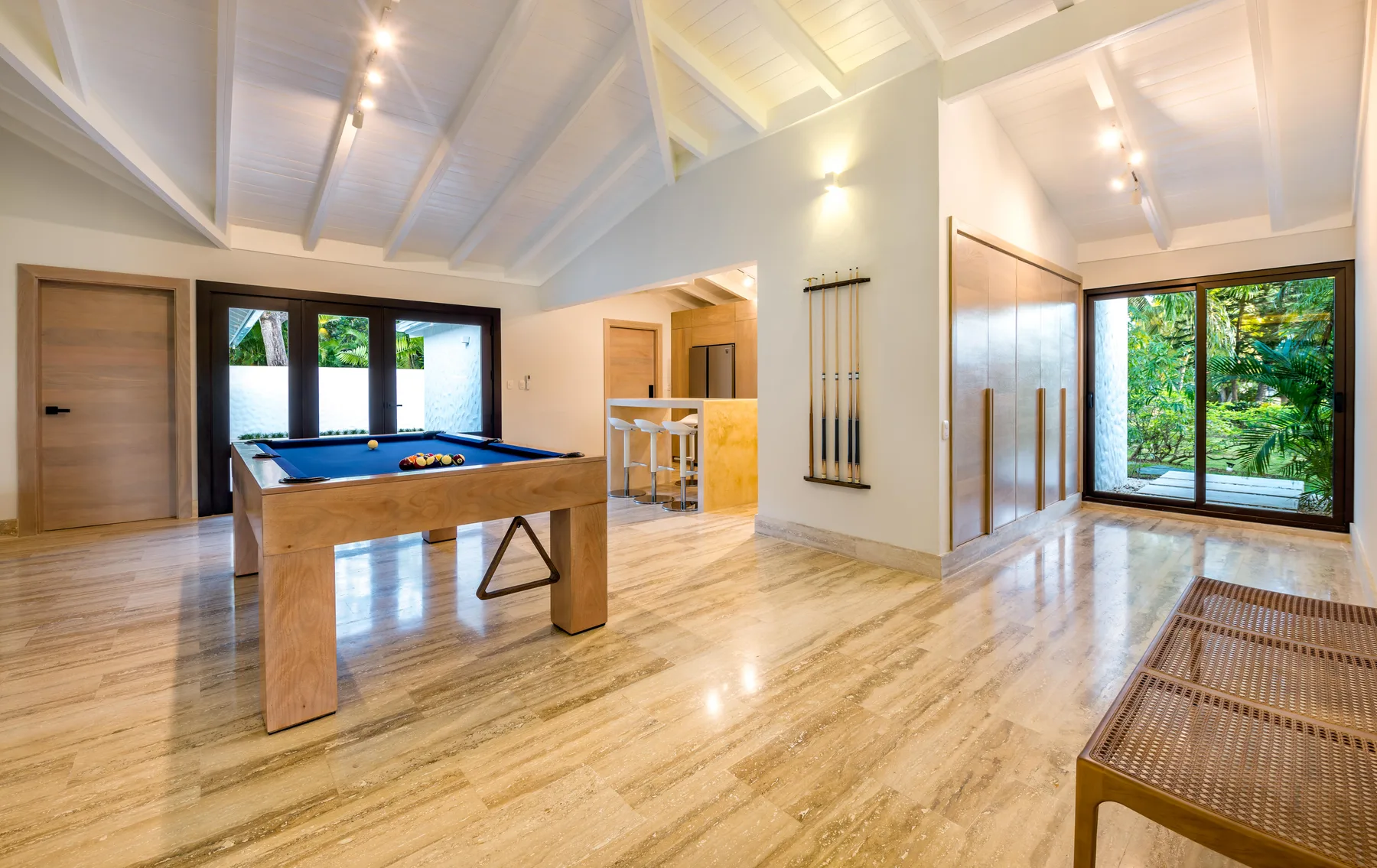 A bright game room features a pool table and large windows overlooking greenery.