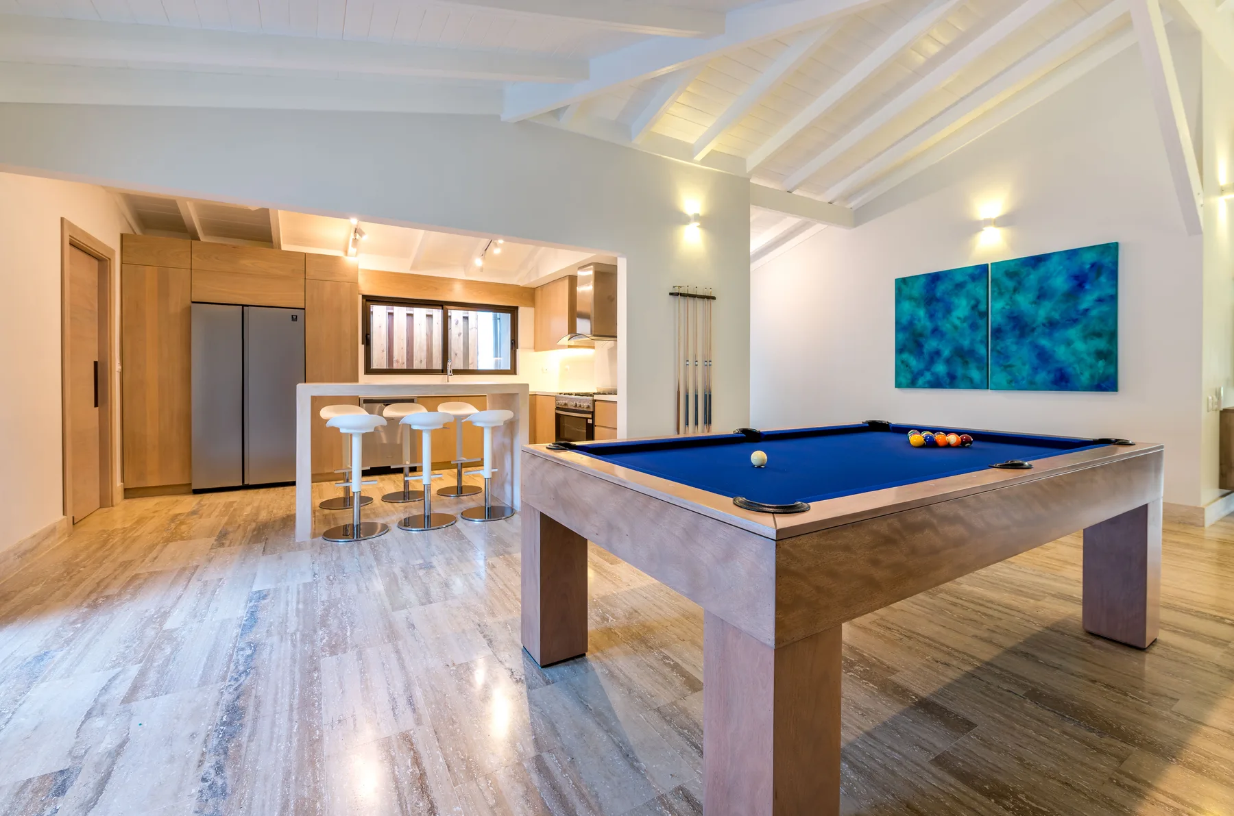 A billiards table fills a bright open room beside a kitchen and counter seating.