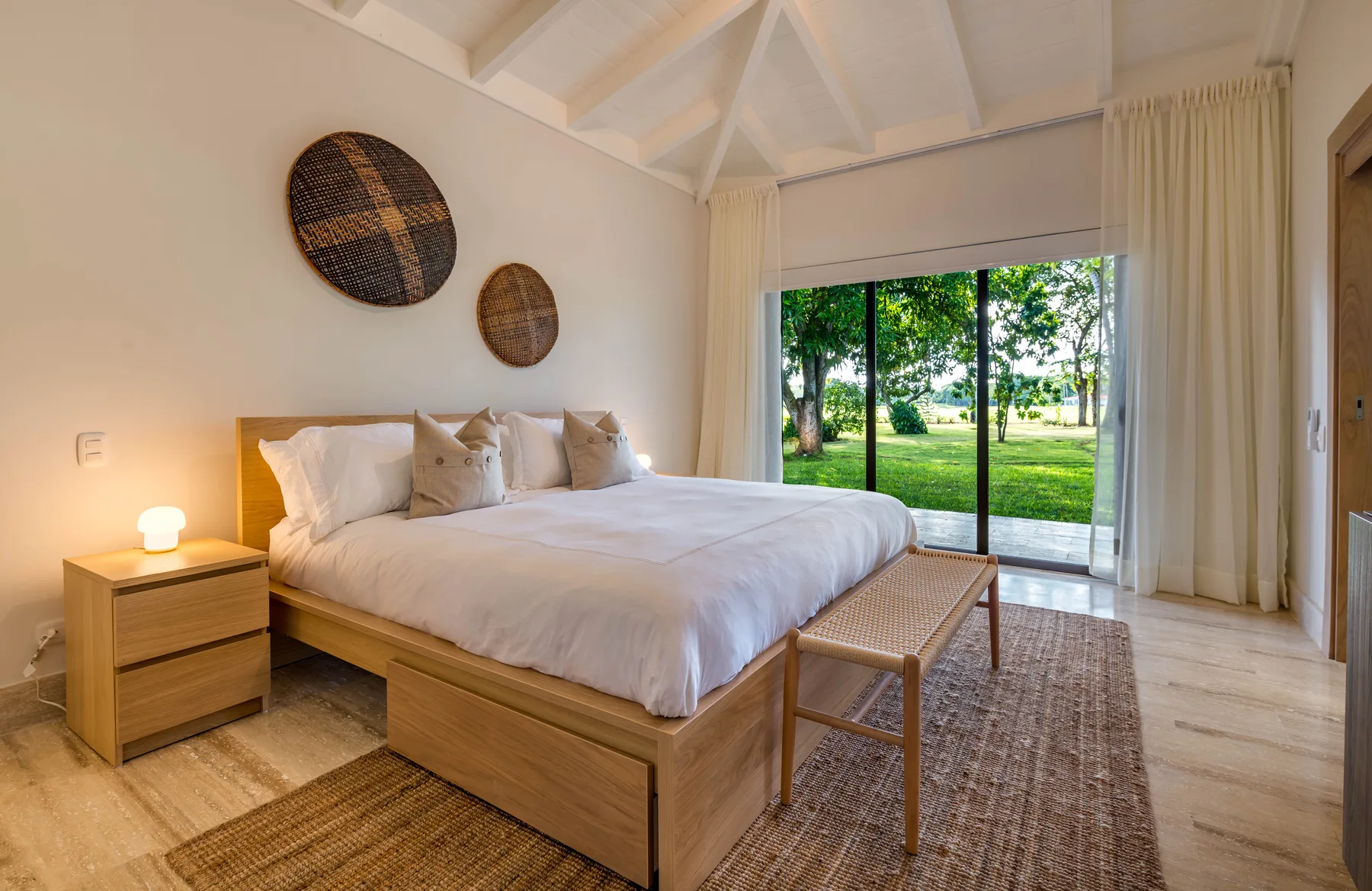 A bright bedroom with a large bed facing glass doors and a garden.