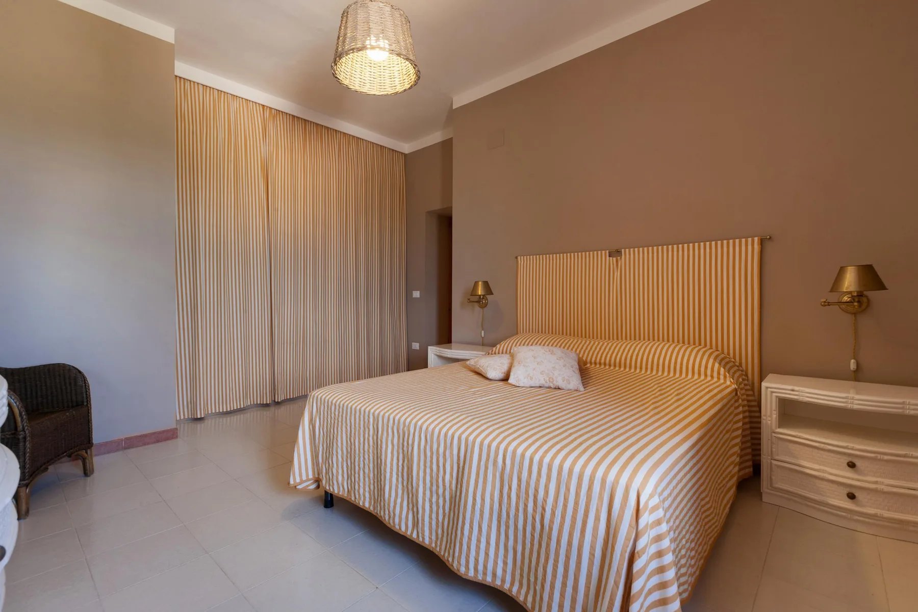 A bedroom with a striped bedspread, tall curtains, and bedside lamps.