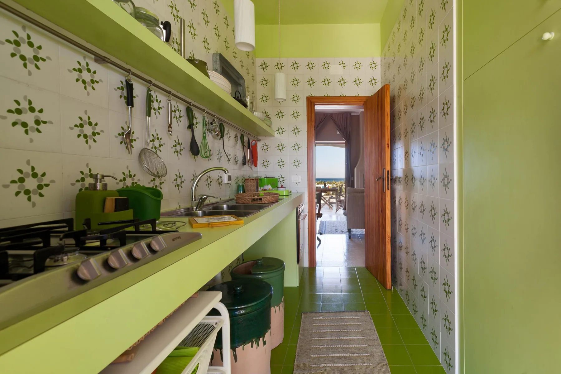 A narrow kitchen with green counters, a cooktop, and patterned wall tiles.