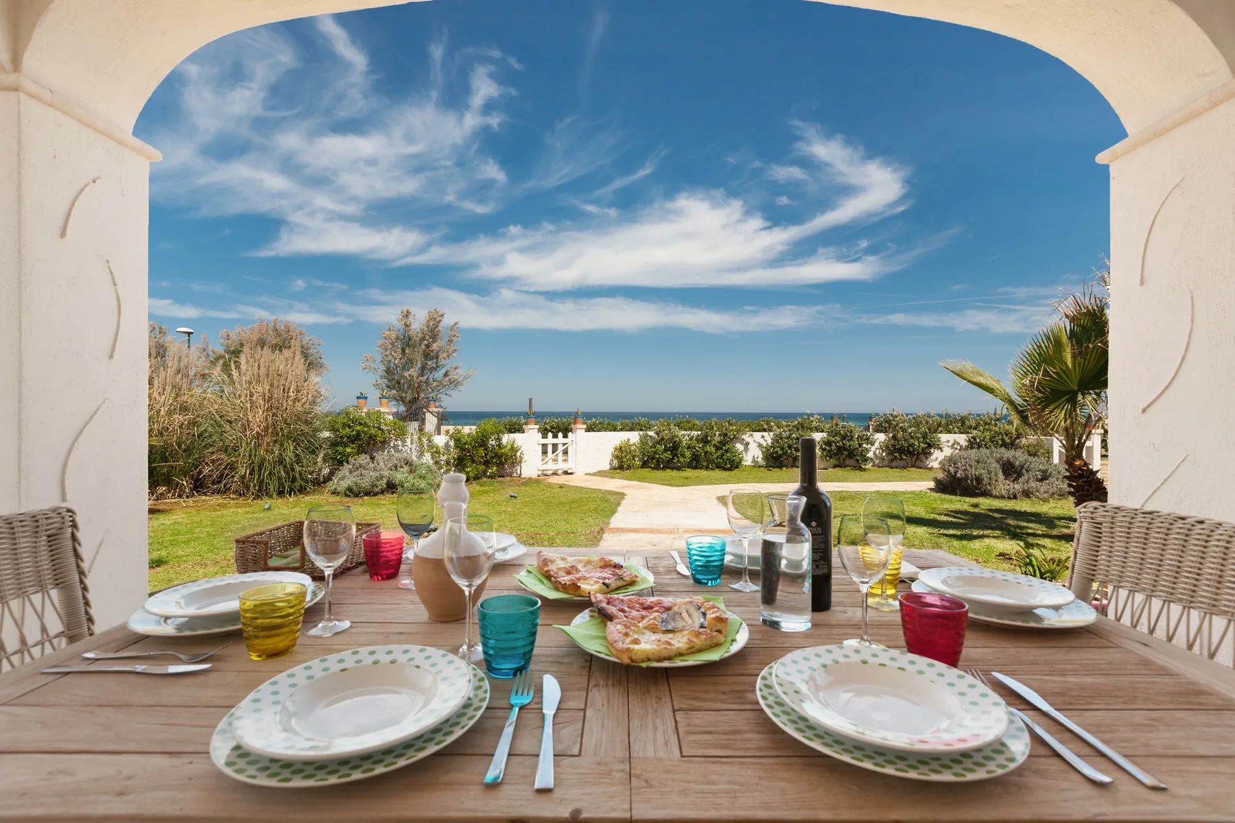 A garden dining area overlooks the sea, with a set table beneath an arch.
