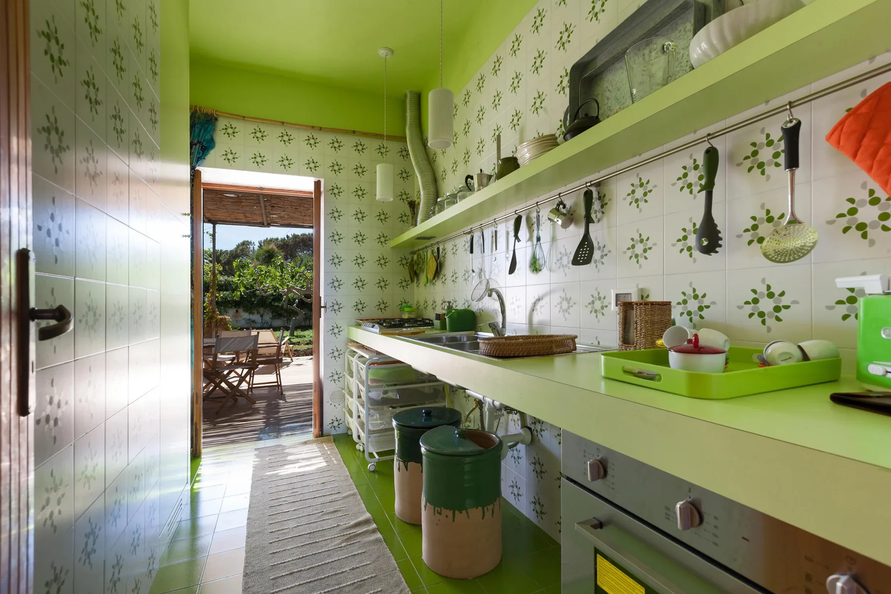A narrow kitchen with green countertops and utensils hanging on the wall.