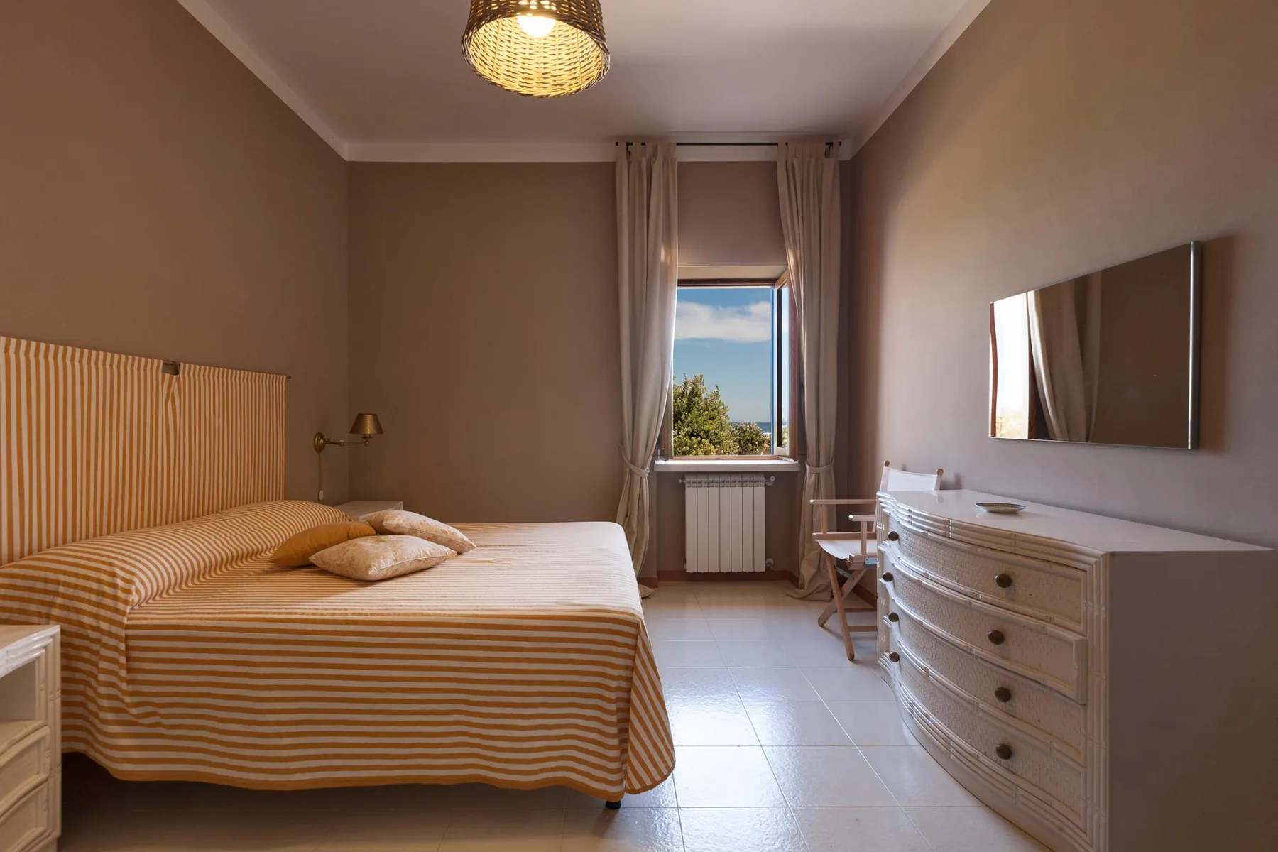 A bedroom with a striped bed, a window, and a dresser.
