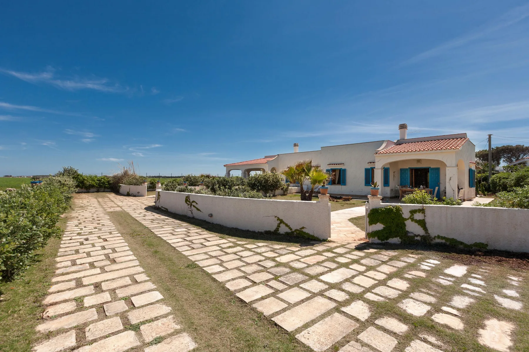 A white house with blue shutters sits beyond a stone-paved garden path.