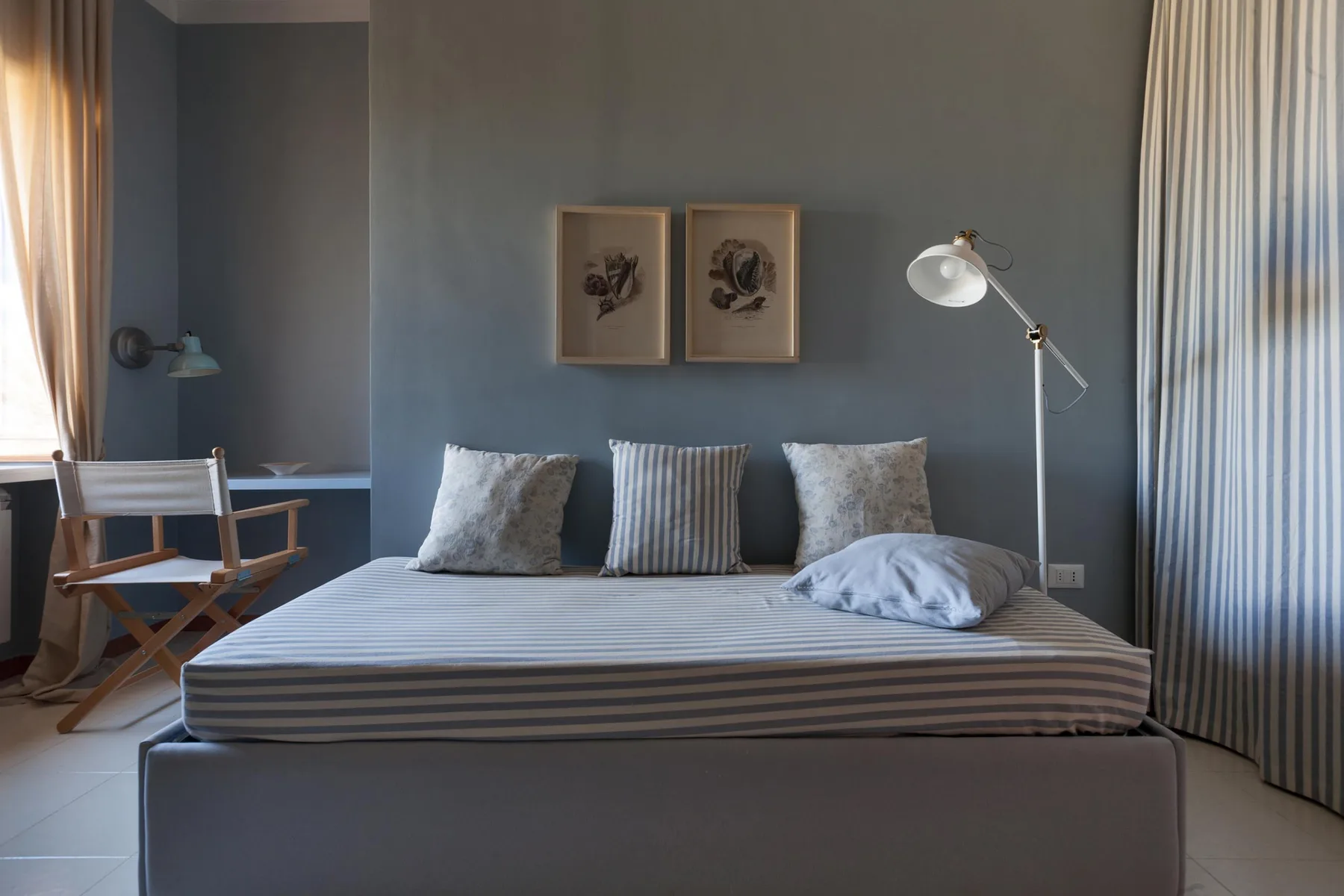 A bedroom with a striped bed and a floor lamp beside it.