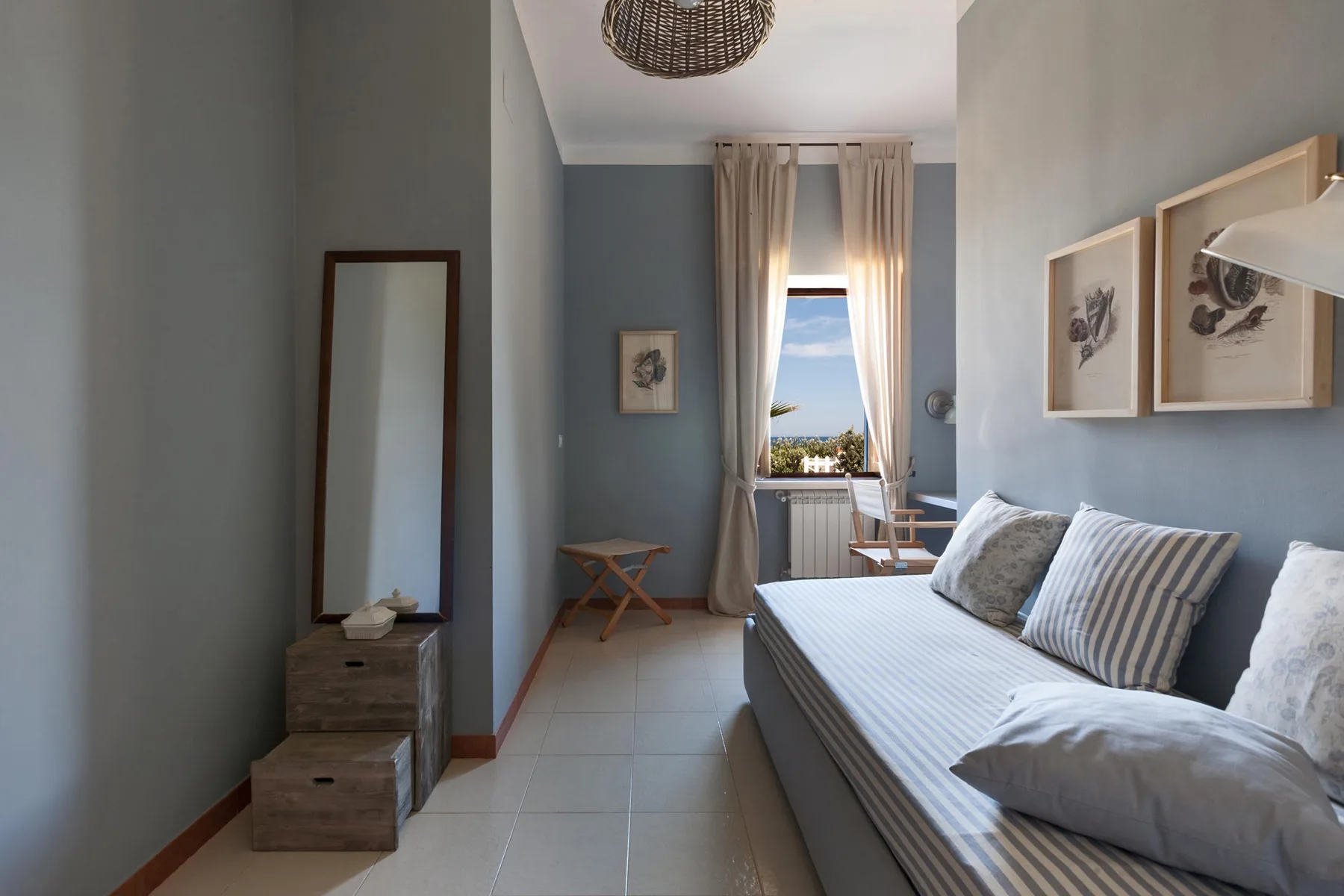 A bedroom with a bed, framed pictures, and a tall window with curtains.