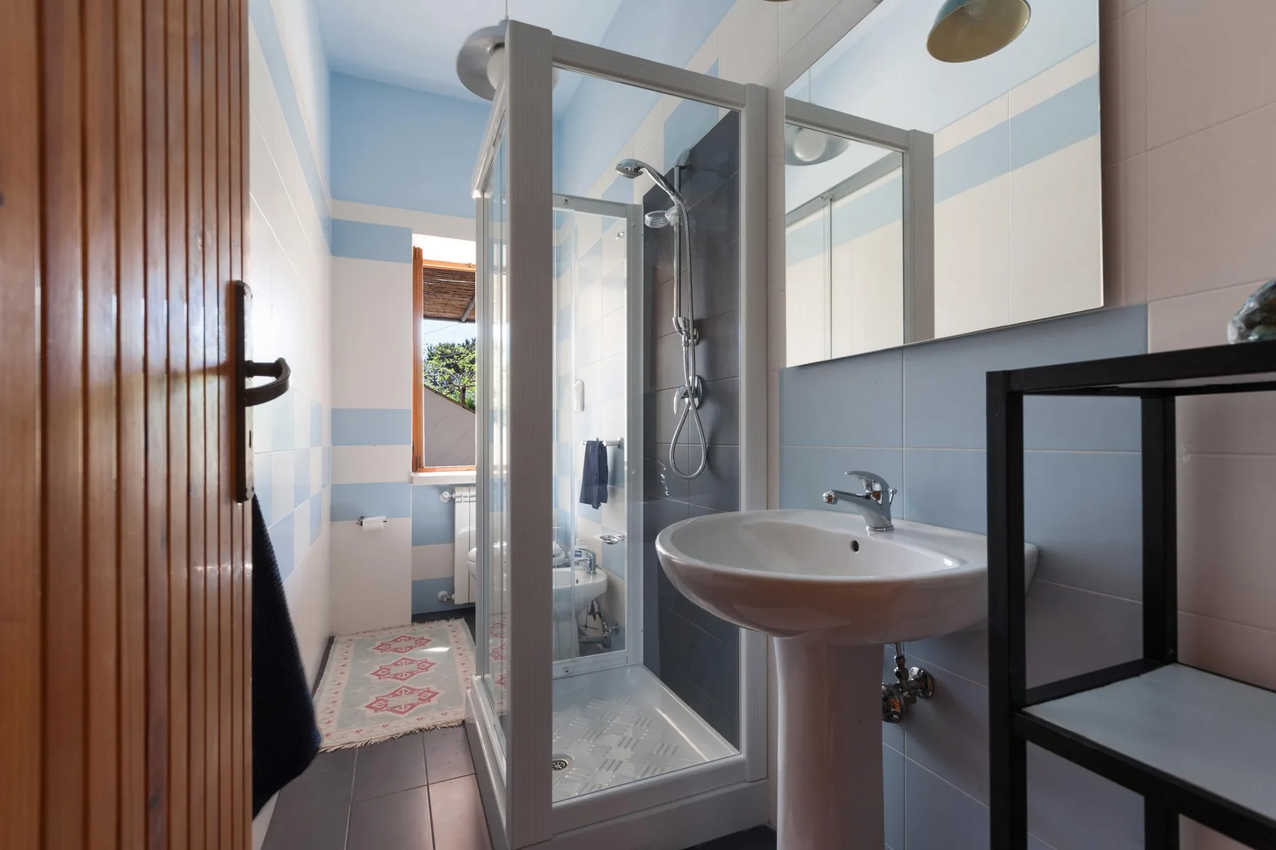 A bathroom with a glass shower, pedestal sink, and blue-and-white tiled walls.