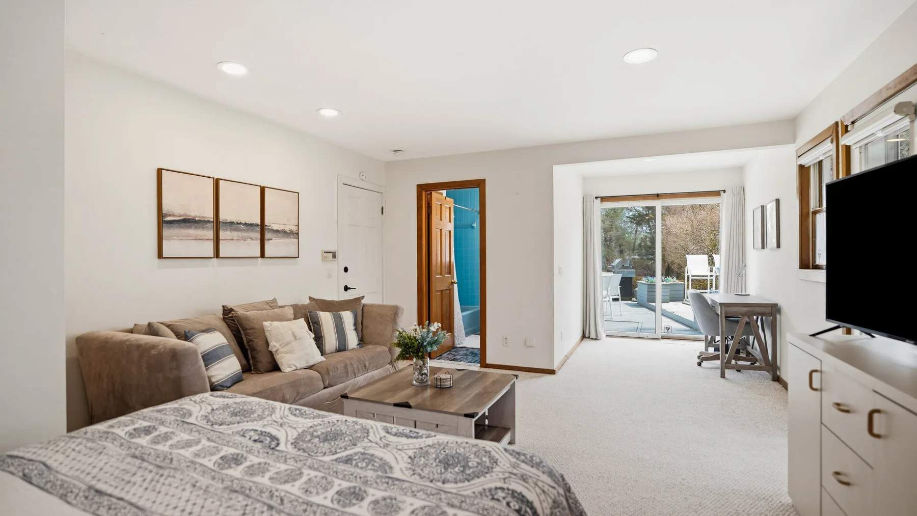 A bright living room with seating, a coffee table, and a bed in the foreground.