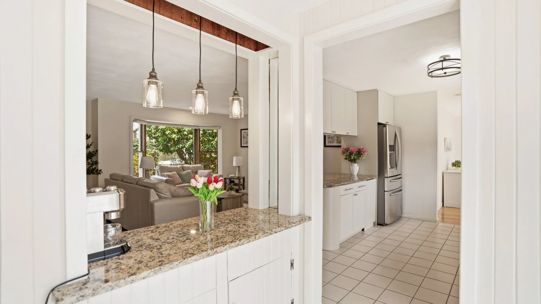 An open kitchen with a stone countertop overlooks a living area.