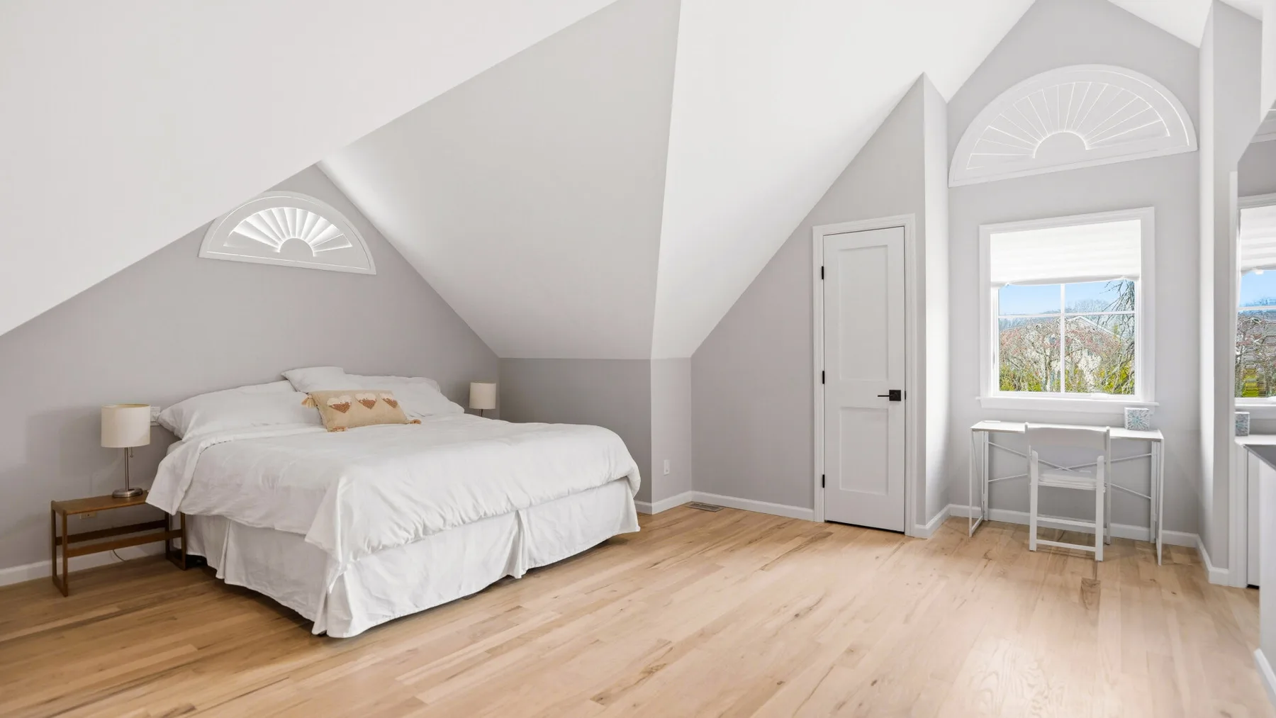 A bright attic bedroom with a bed, sloped ceilings, and a desk by the window.