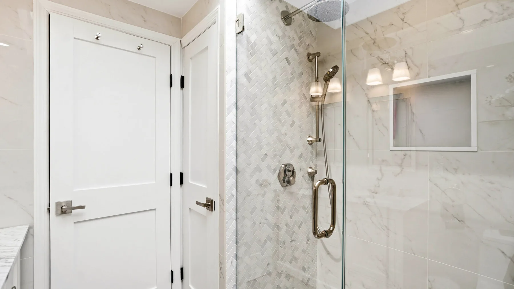 A tiled bathroom with a glass shower and white doors.