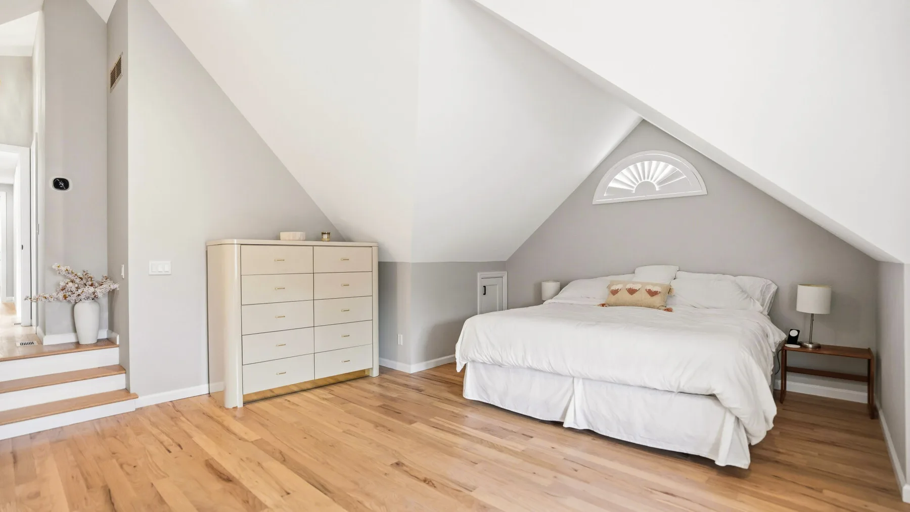 A bright attic bedroom with a bed beneath a sloped ceiling and a wooden floor.
