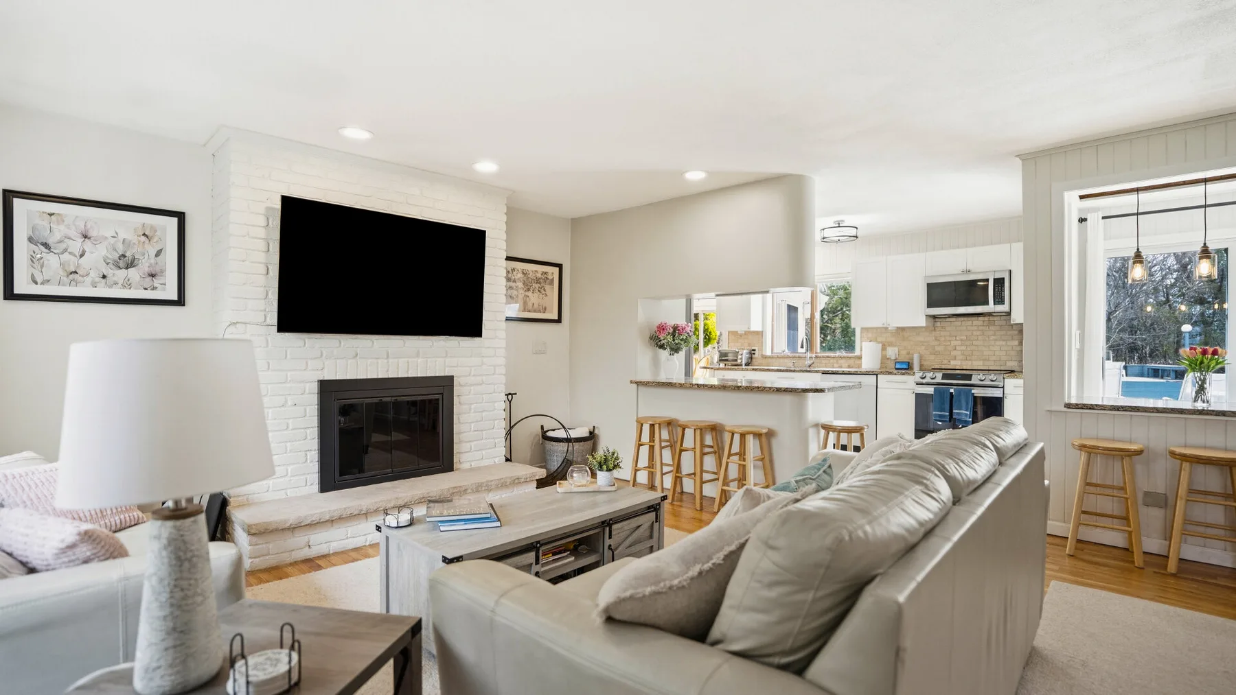 A bright living room opens into a kitchen, with a fireplace and island seating.