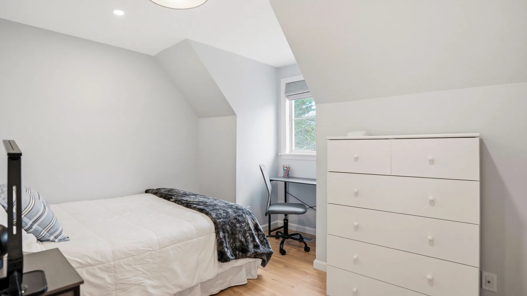 A bedroom with a bed, dresser, and window under a sloped ceiling.