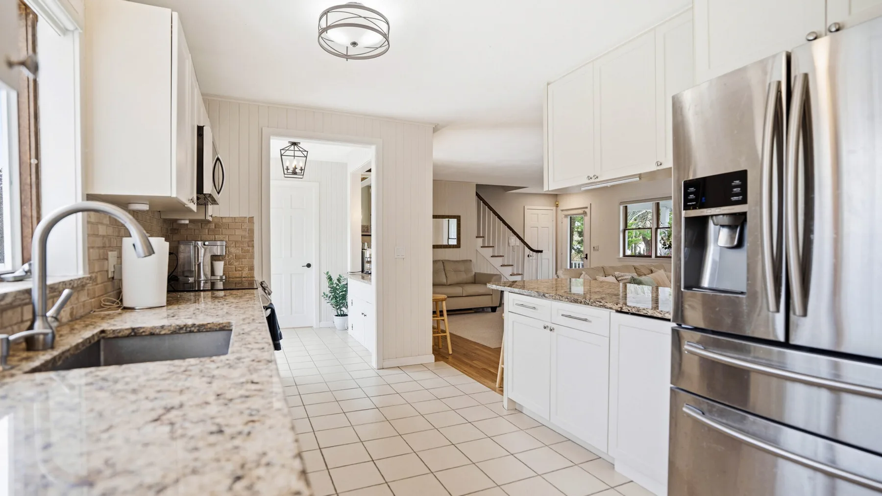 A bright kitchen with white cabinets, stone counters, and a stainless steel refrigerator.