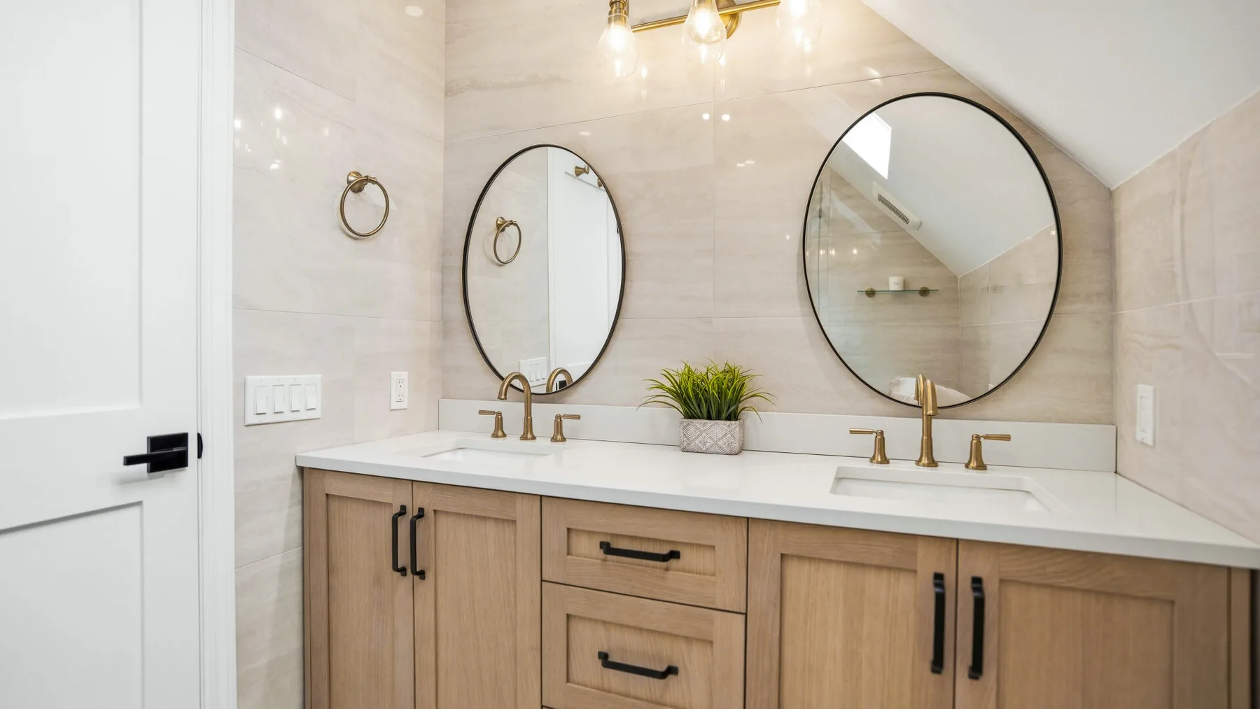 A bright bathroom vanity with two sinks, round mirrors, and wood cabinetry.
