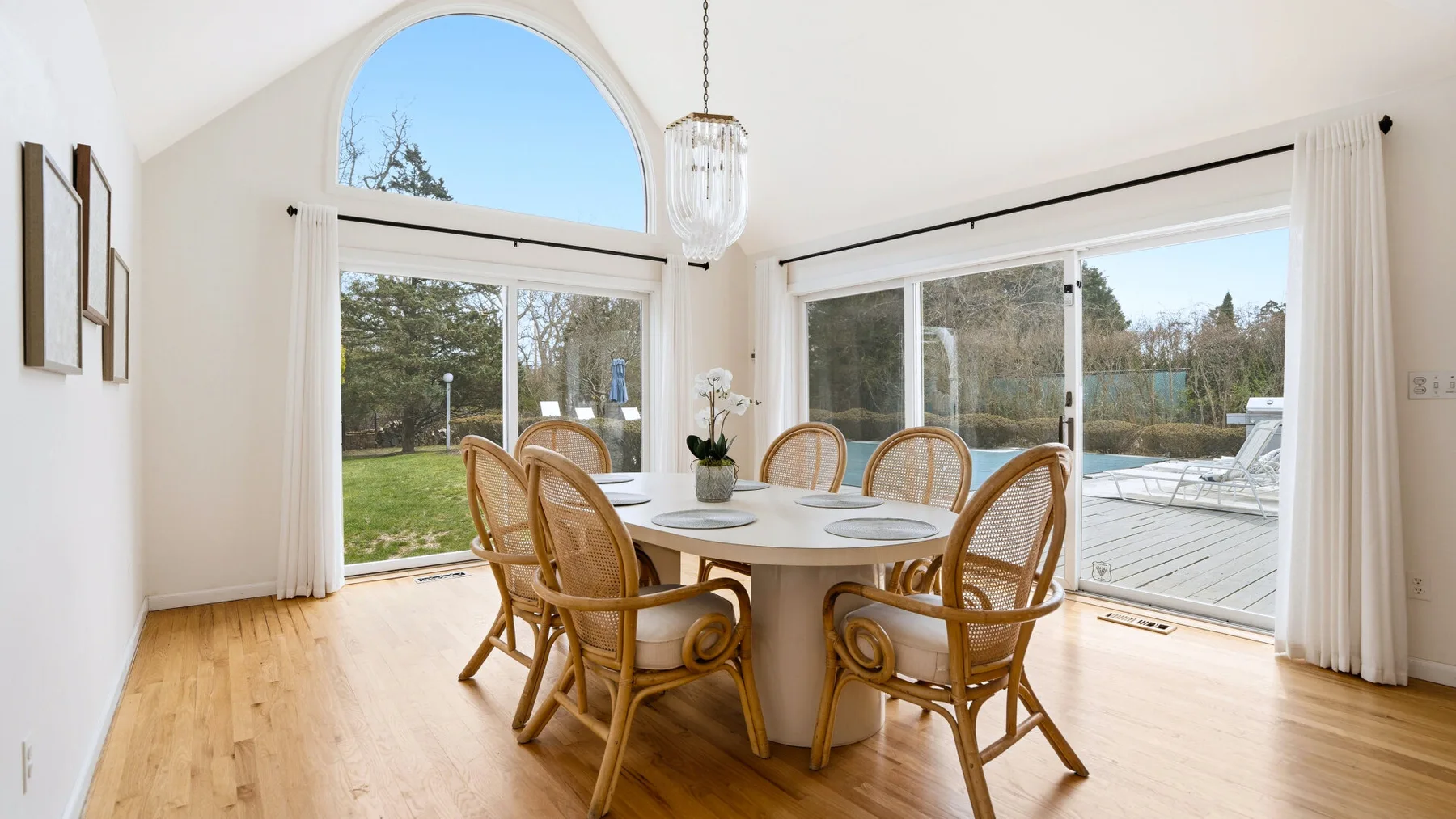 A dining area with a round table and wicker seating beside large windows.