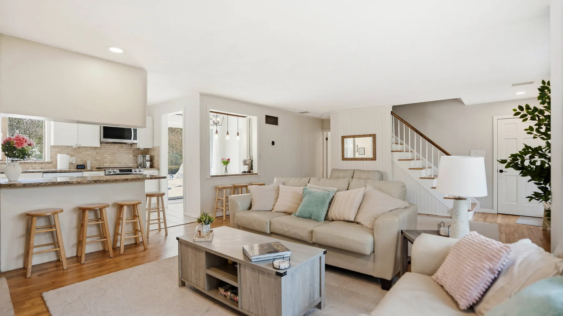 An open-plan living room with beige seating, a coffee table, and a kitchen counter.