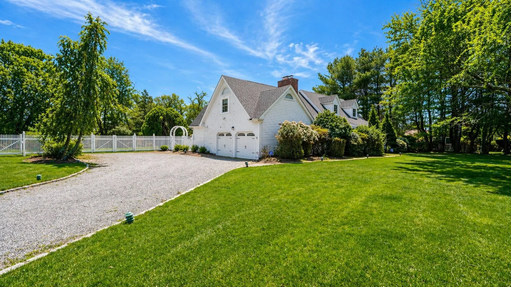 A white house with a gravel driveway sits beside a broad green lawn.