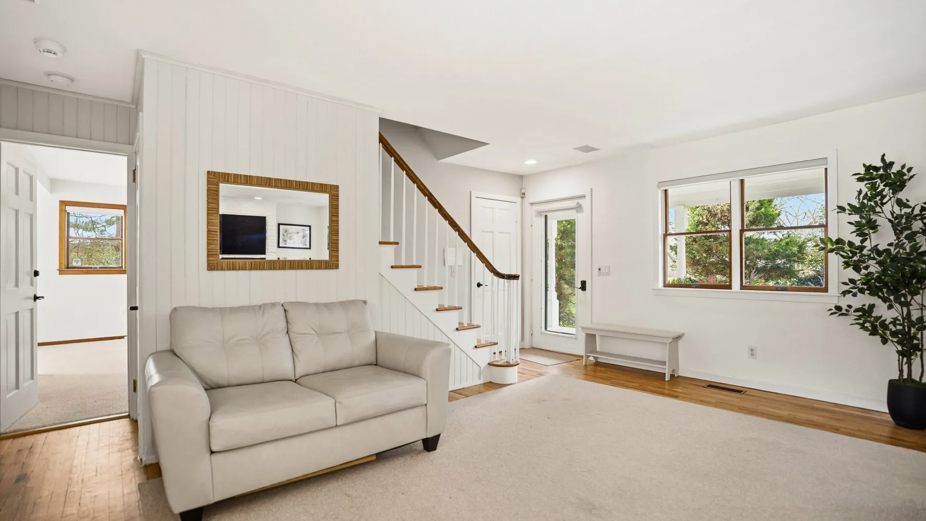 A bright living room with a sofa, staircase, and large windows.