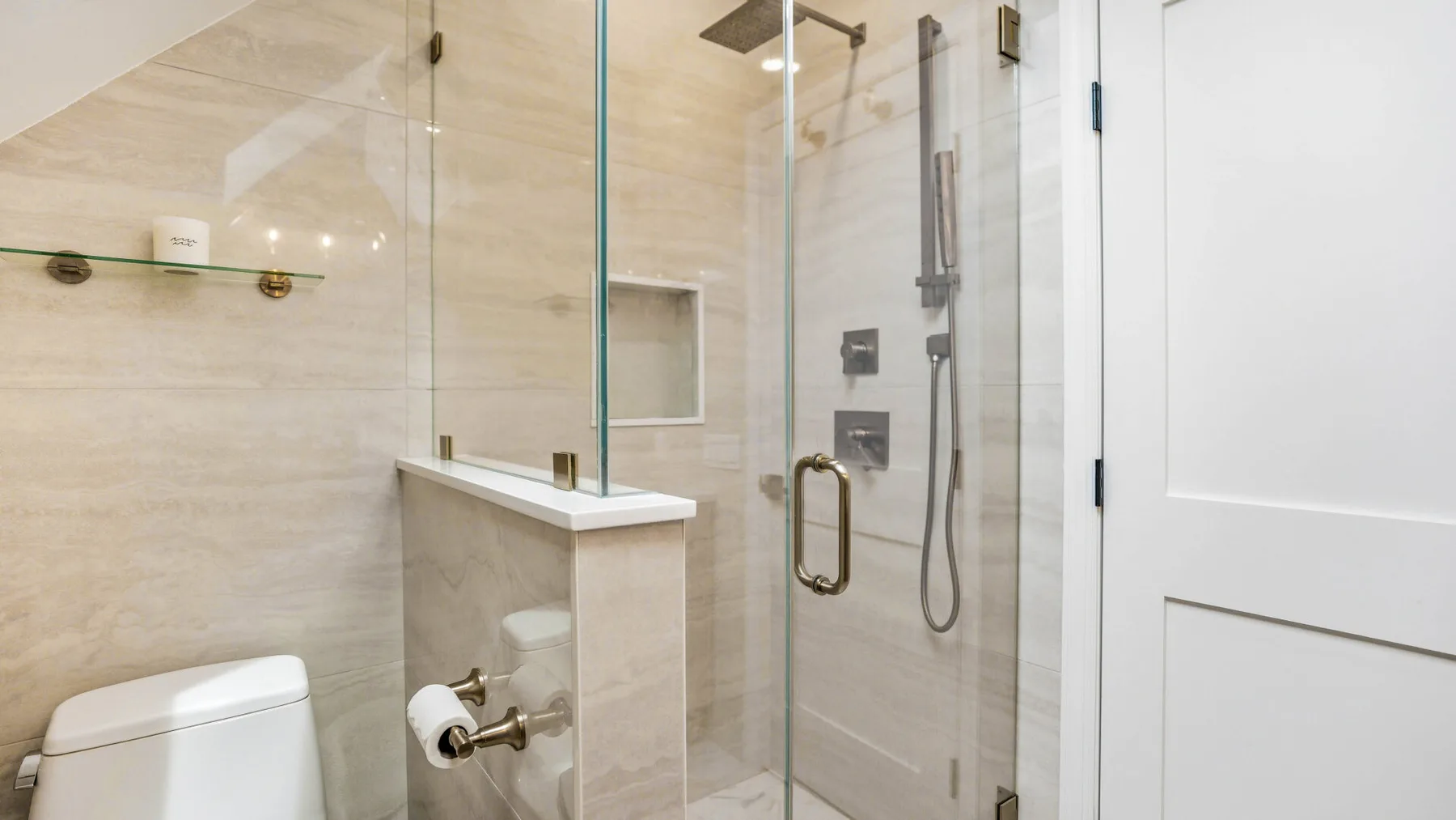 A tiled bathroom with a glass shower enclosure and a toilet.