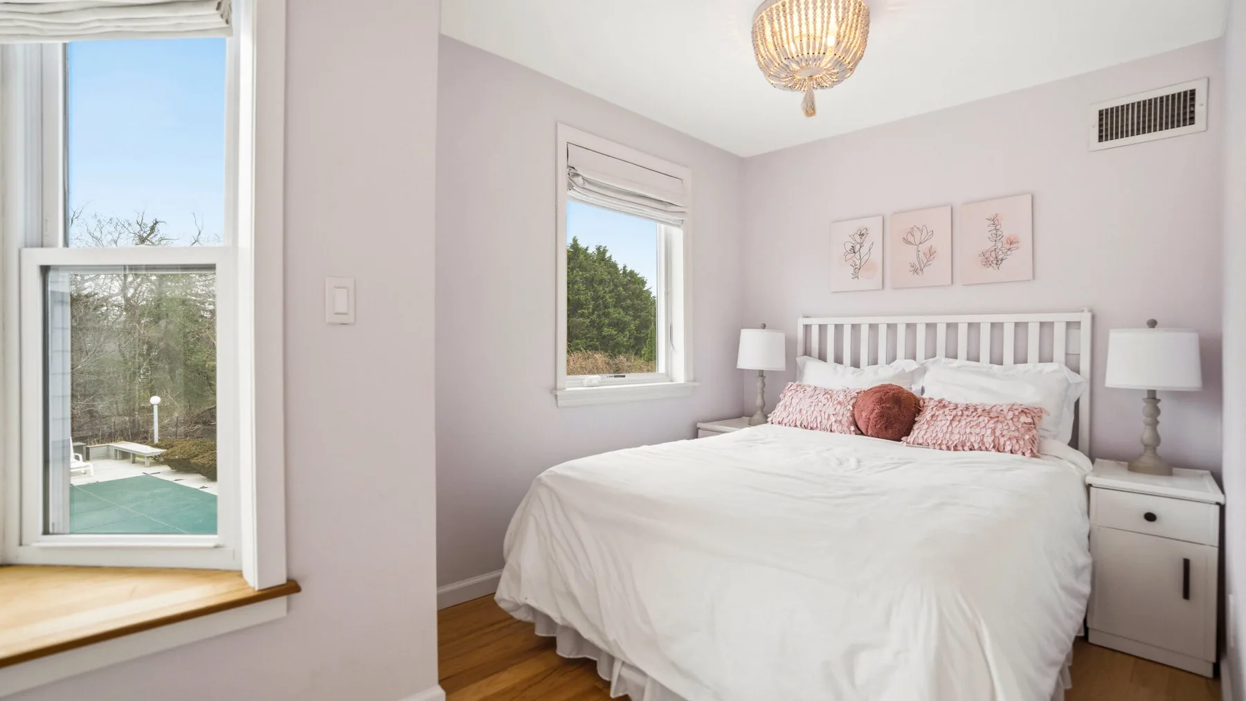 A bright bedroom with a neatly made bed and windows overlooking greenery.