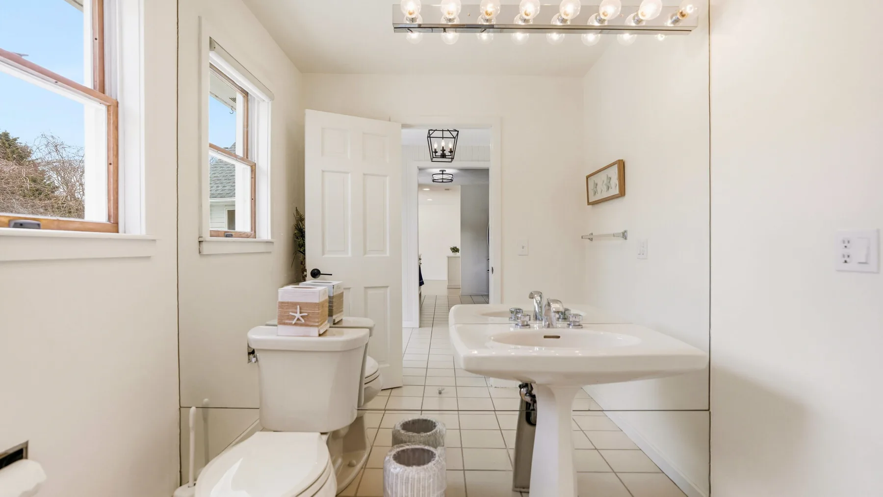 A bright bathroom with a pedestal sink, toilet, and tiled floor.