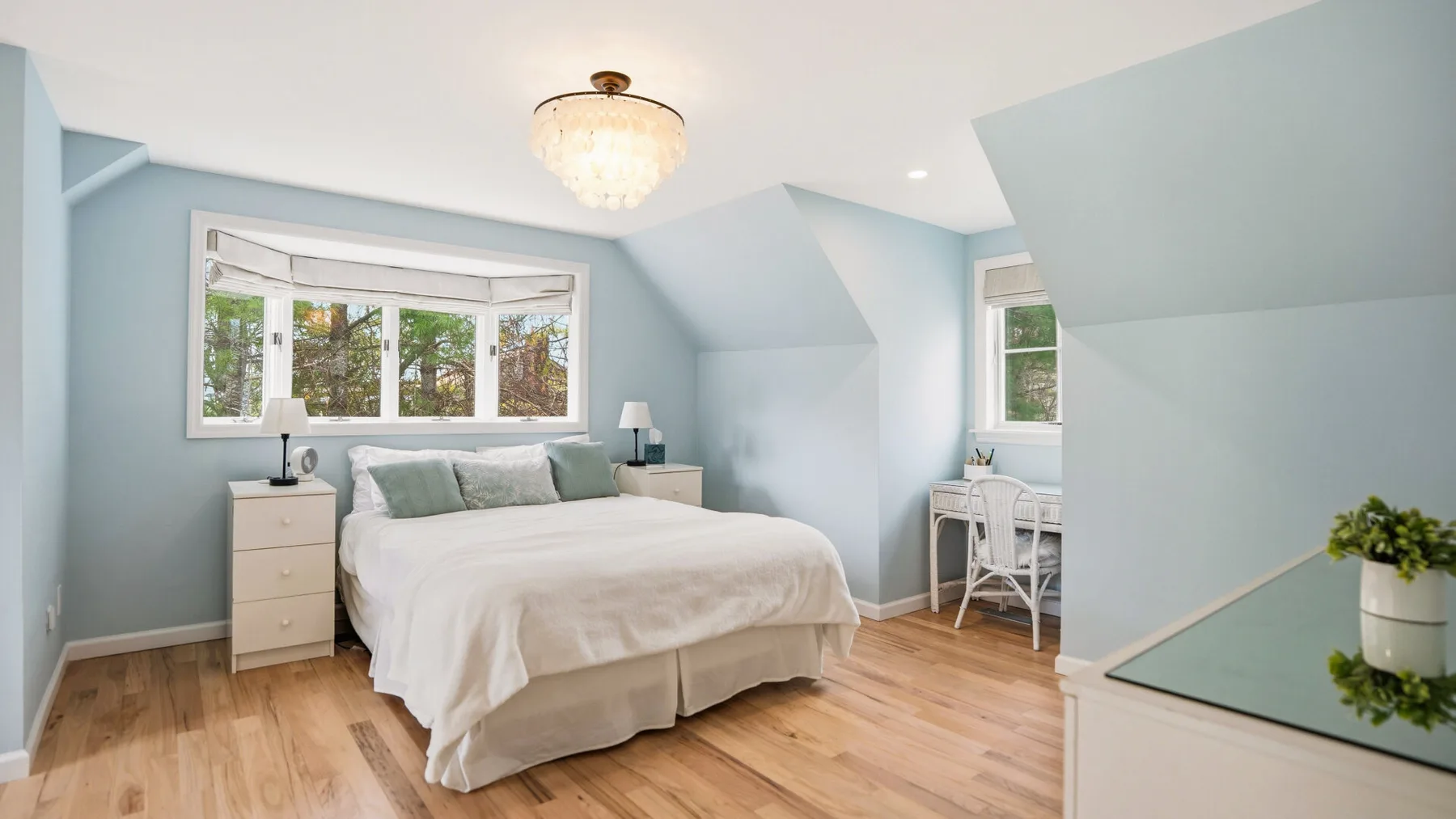 A bright bedroom with a bed and a small desk beside the window.
