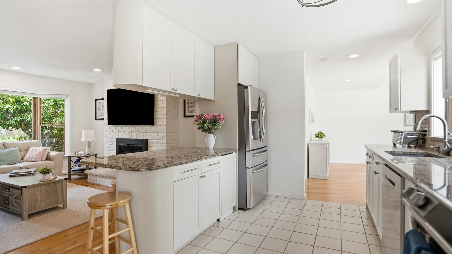 A bright open-plan kitchen and living area with white cabinetry and a dining island.