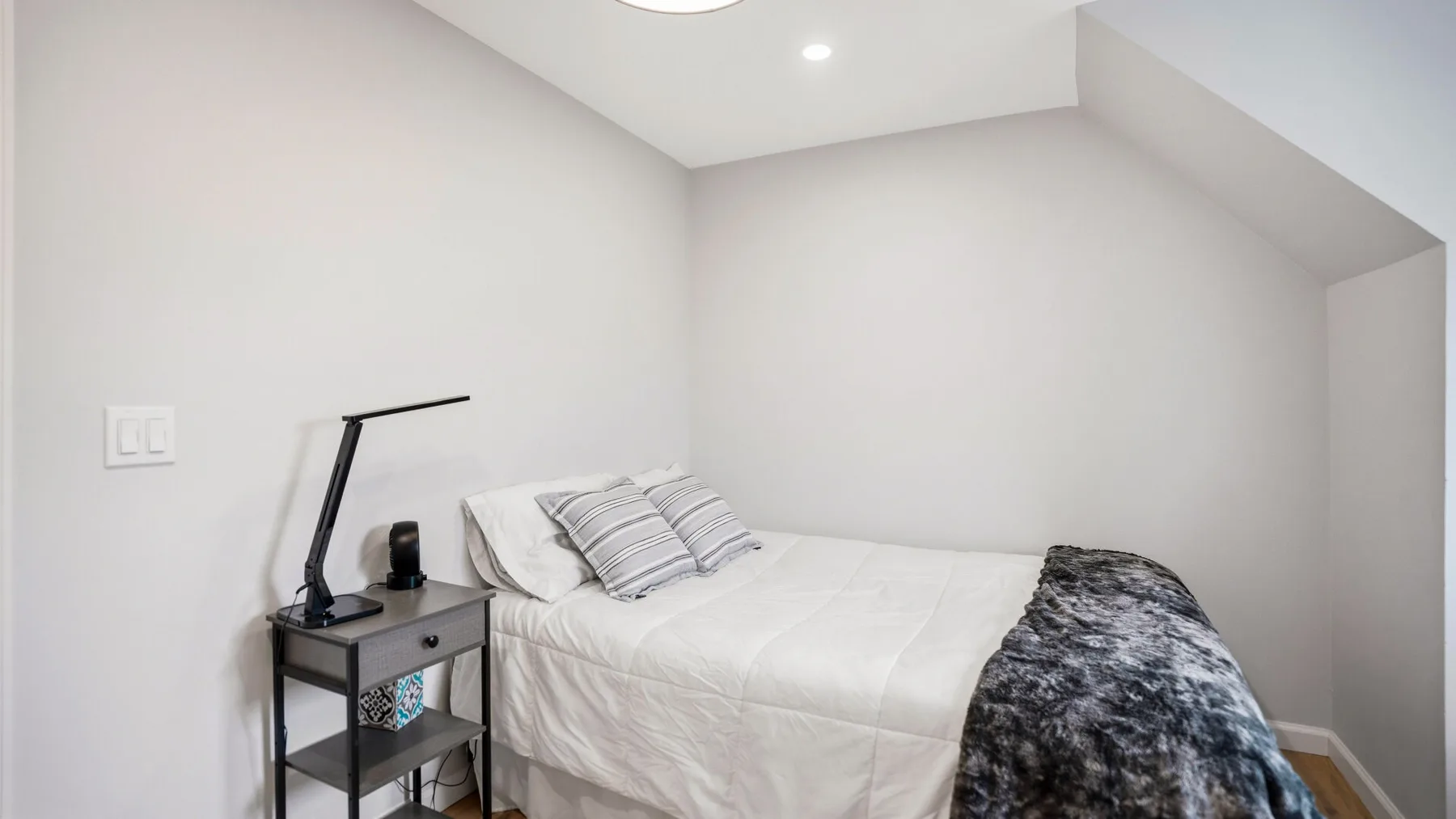 A bright bedroom with a neatly made bed and a bedside table.