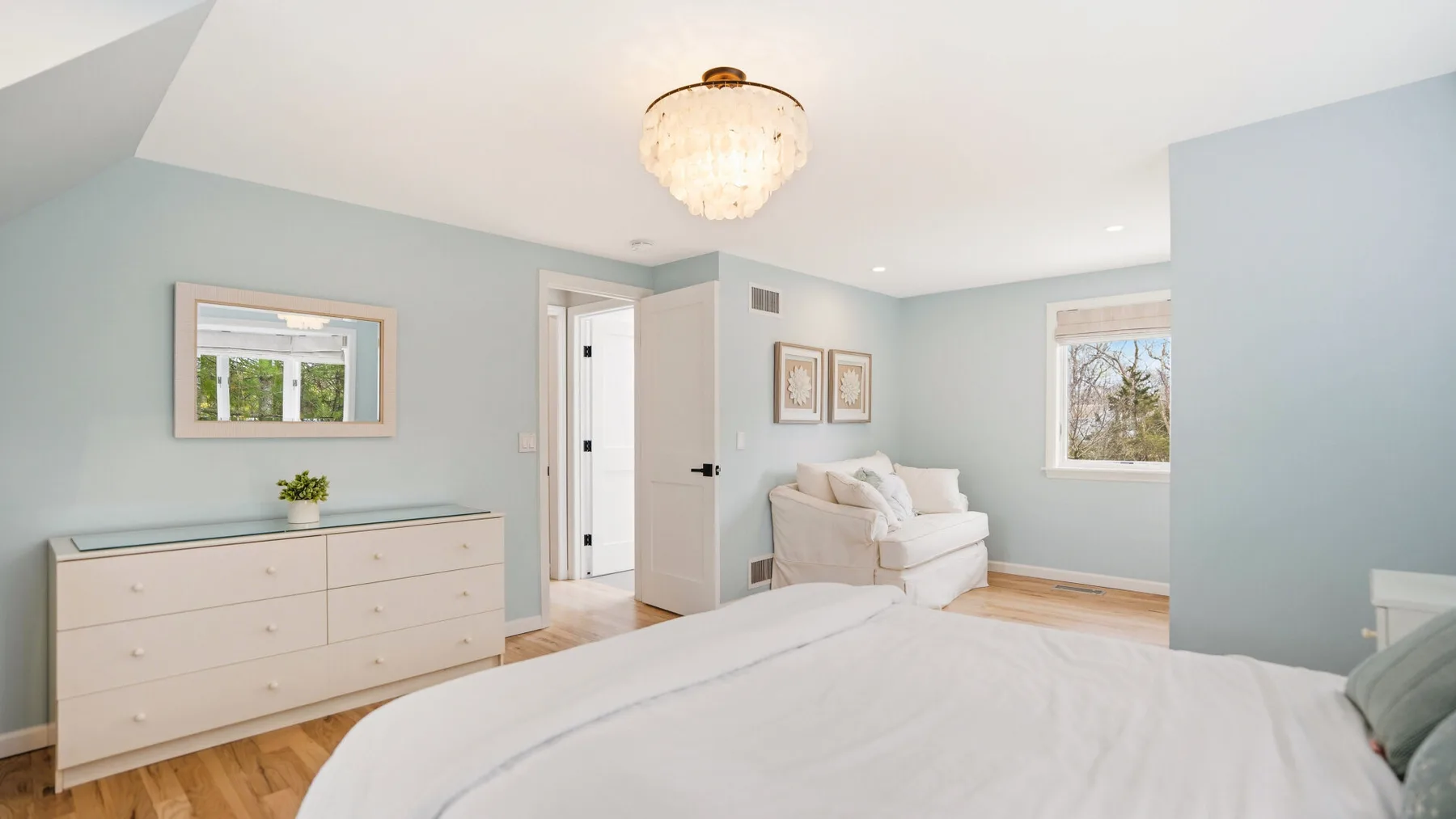 A bright bedroom with a white bed, dresser, and upholstered seating.