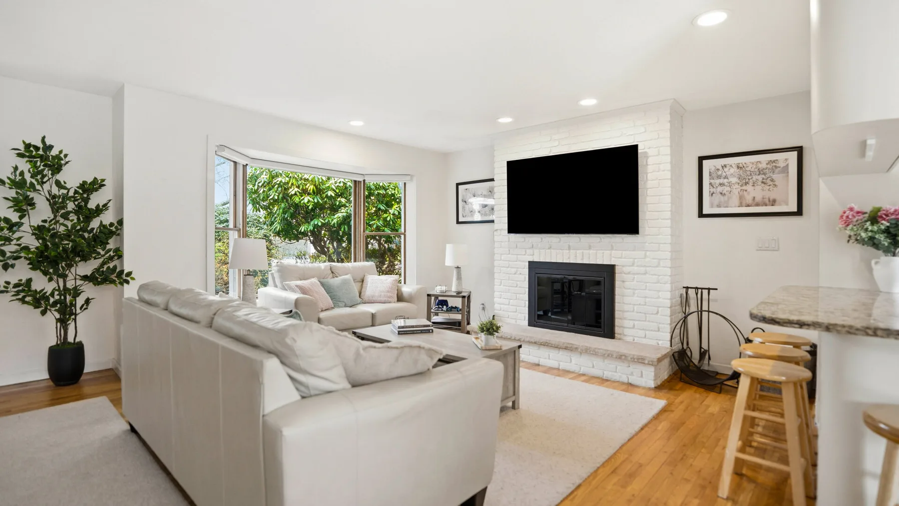 A bright living room with light seating facing a television above a fireplace.